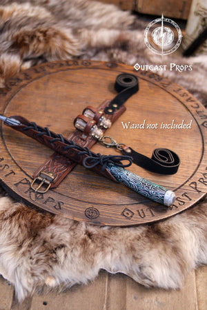Brown leather wand holster garter displayed on fur background, opened to show all parts: embossed leather panel, thigh strap, bottle holders and lace-up wand sheath. A wooden wand rests inside (not included). Clear product layout for brown leather wizard garter, potion holster for thigh, LARP fantasy leg harness for wands and vials.