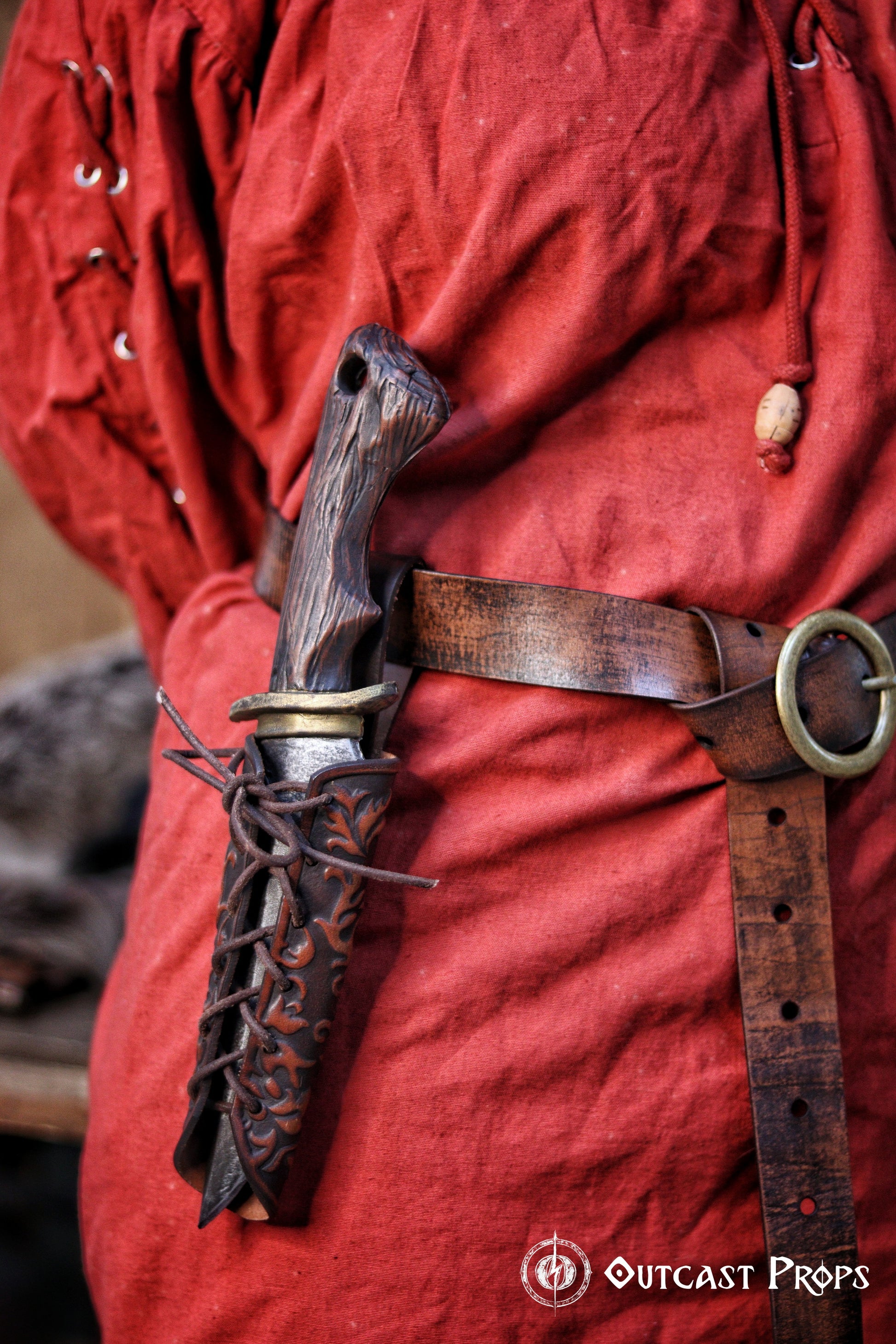 A leather dagger sheath with embossed details, laced closure, and a belt loop, attached to a red costume. Handmade leather dagger sheath | Ornate LARP scabbard | Viking, medieval, fantasy belt holster for daggers | Ren Faire cosplay accessory