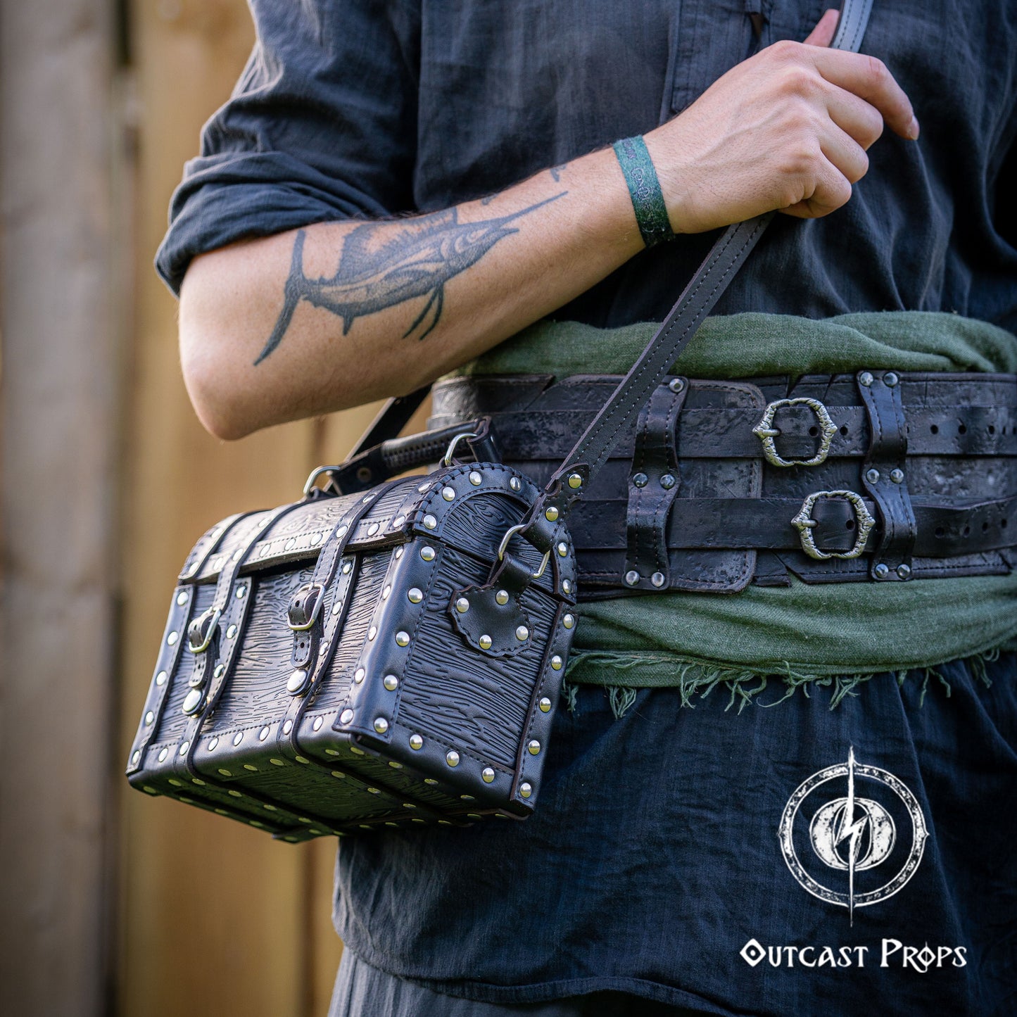 Person wearing a belt with a leather pouch, with 'Outcast Props' logo. Person holding a black leather bag with studs outdoors, featuring 'Outcast Props' logo. Person wearing a dark outfit with a leather bag, holding a belt with multiple buckles. Man wearing a pirate chest leather bag with studs, standing outdoors. Leather treasure chest pirate chest bag larp pirate backpack treasure chest purse pirate accessories cosplay renfaire pouch belt bag