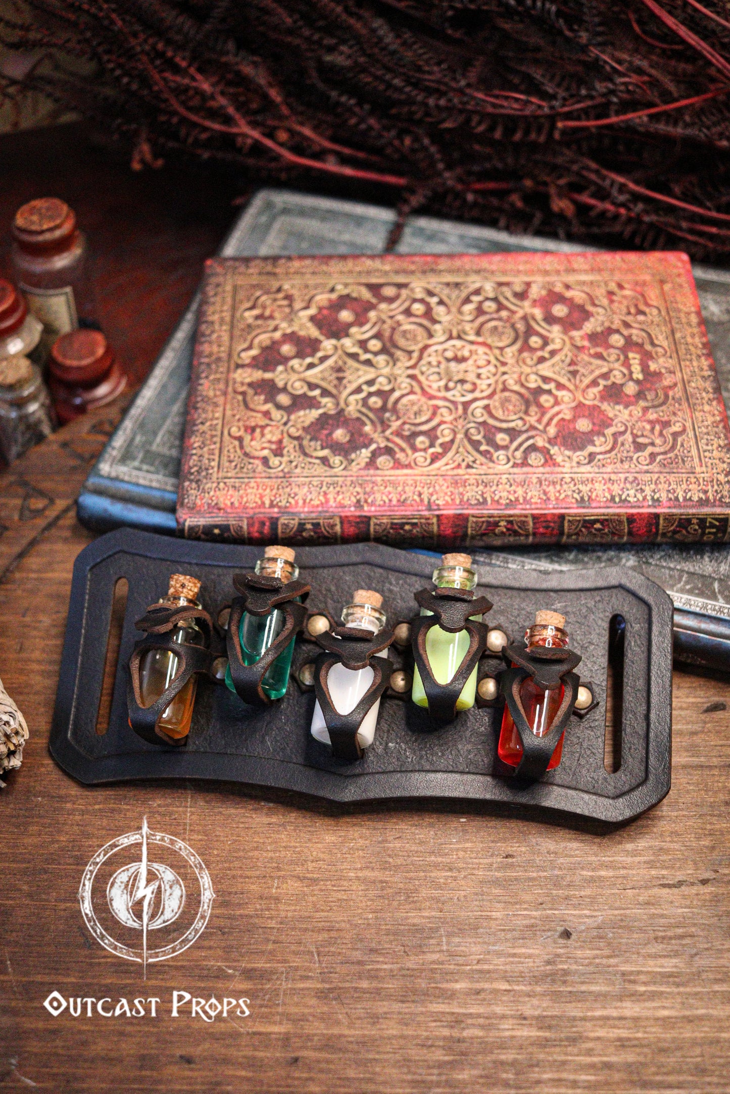 Set of small bottles on a black holster with an ornate book in the background, featuring 'Outcast Props' logo. Belt Potion holder for 5 small bottles. Made of leather for adventurers, steampunk, alchemist, healers, cosplay or just to keep spices