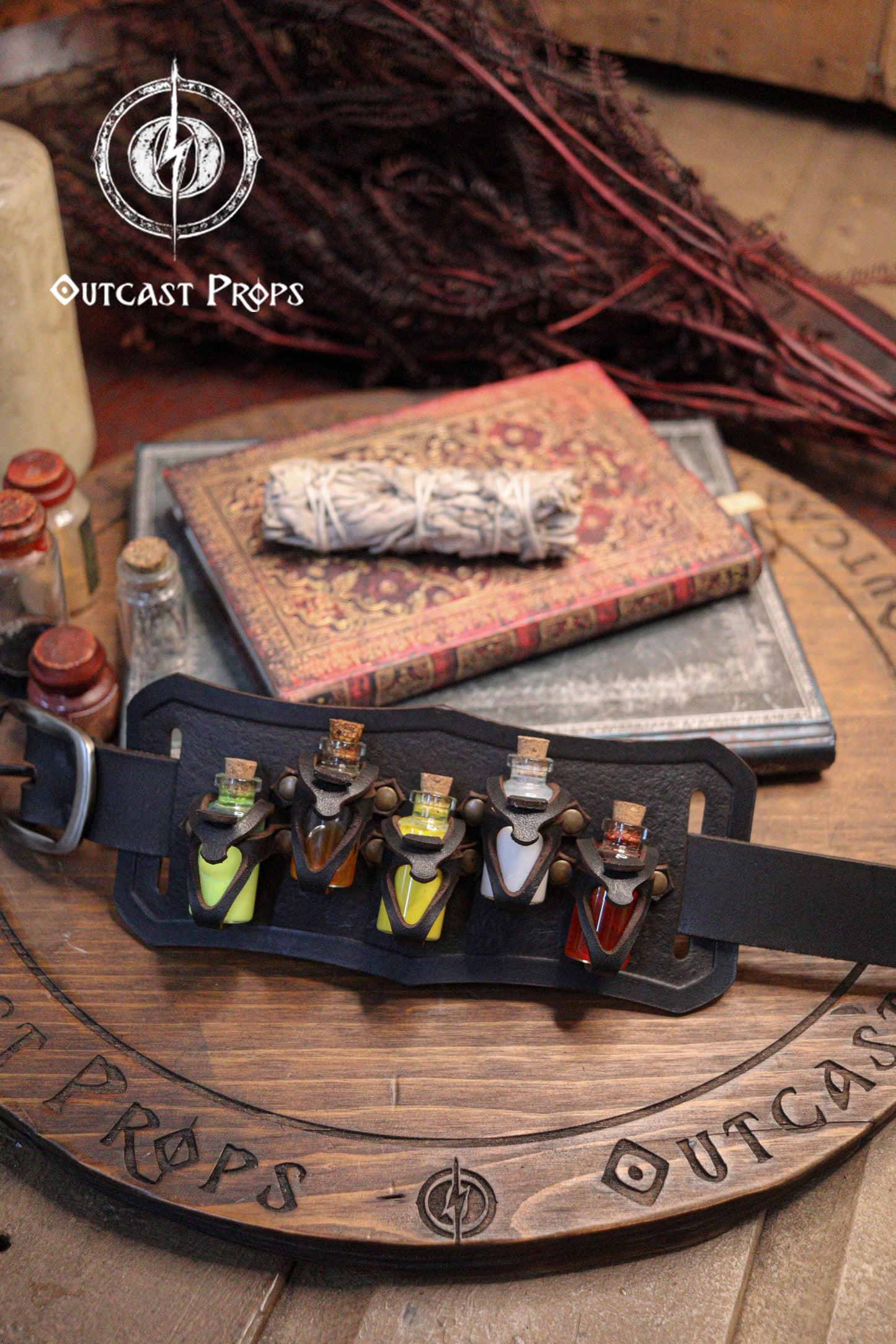 Belt Potion holder for 5 small bottles. Made of leather for adventurers, steampunk, alchemist, healers, cosplay or just to keep spices. Belt with small potions on a wooden surface with 'Outcast Props' branding.