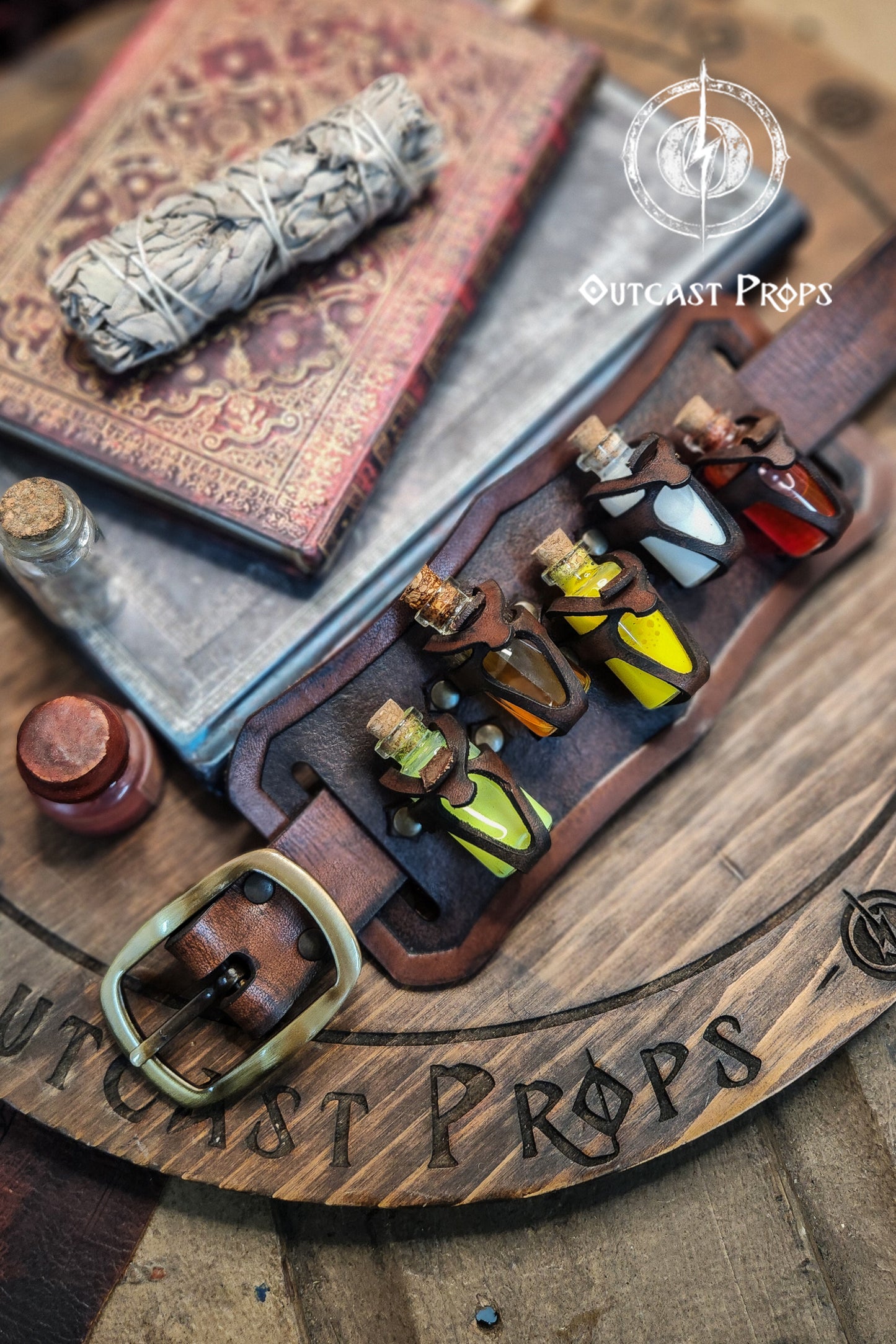 Set of small bottles with colorful liquids on a wooden surface with 'Outcast Props' branding. Belt Potion holder for 5 small bottles. Made of leather for adventurers, steampunk, alchemist, healers, cosplay or just to keep spices