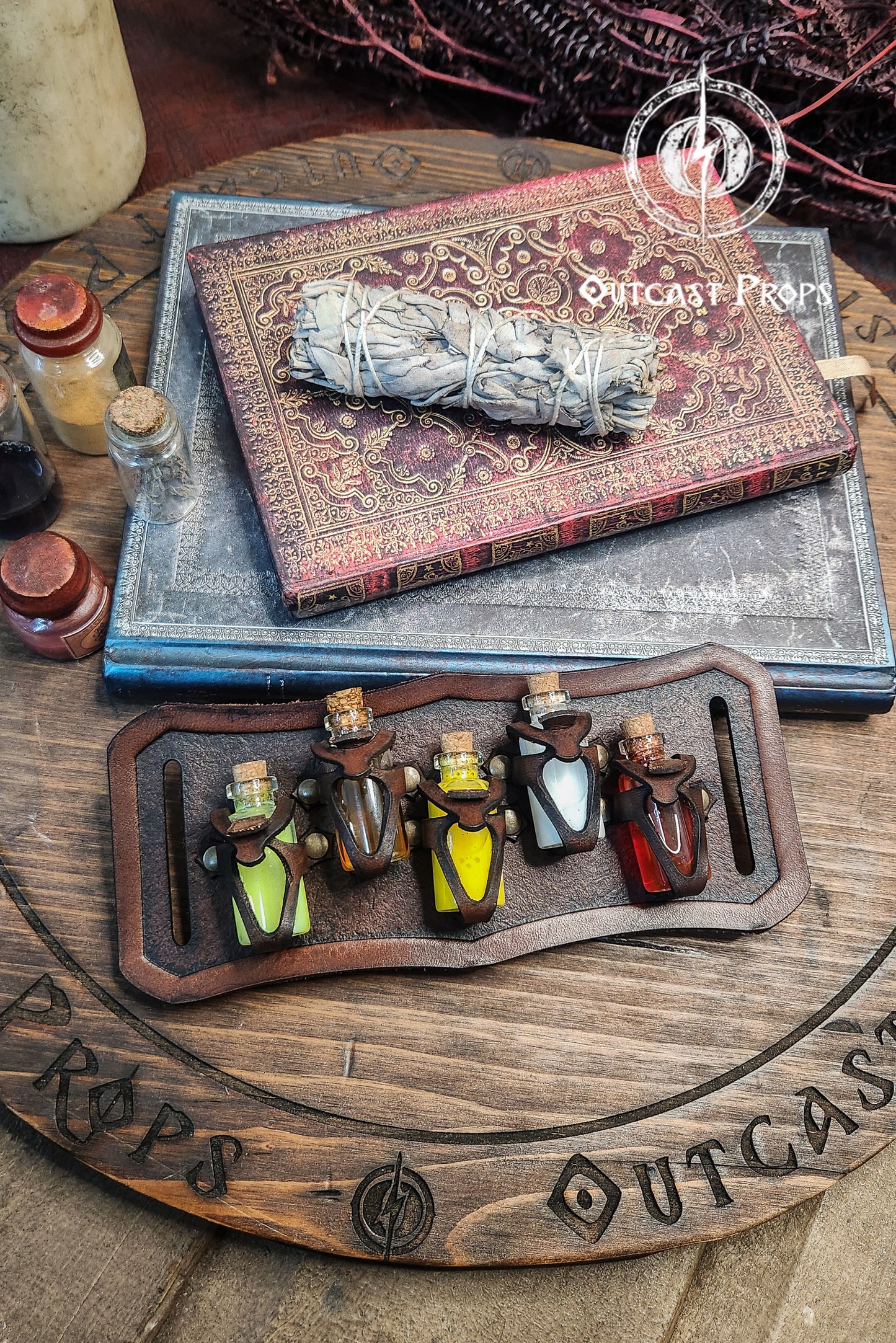 Smoked sage bundle on an old book with 'Outcast Props' branding, surrounded by small bottles. Belt Potion holder for 5 small bottles. Made of leather for adventurers, steampunk, alchemist, healers, cosplay or just to keep spices