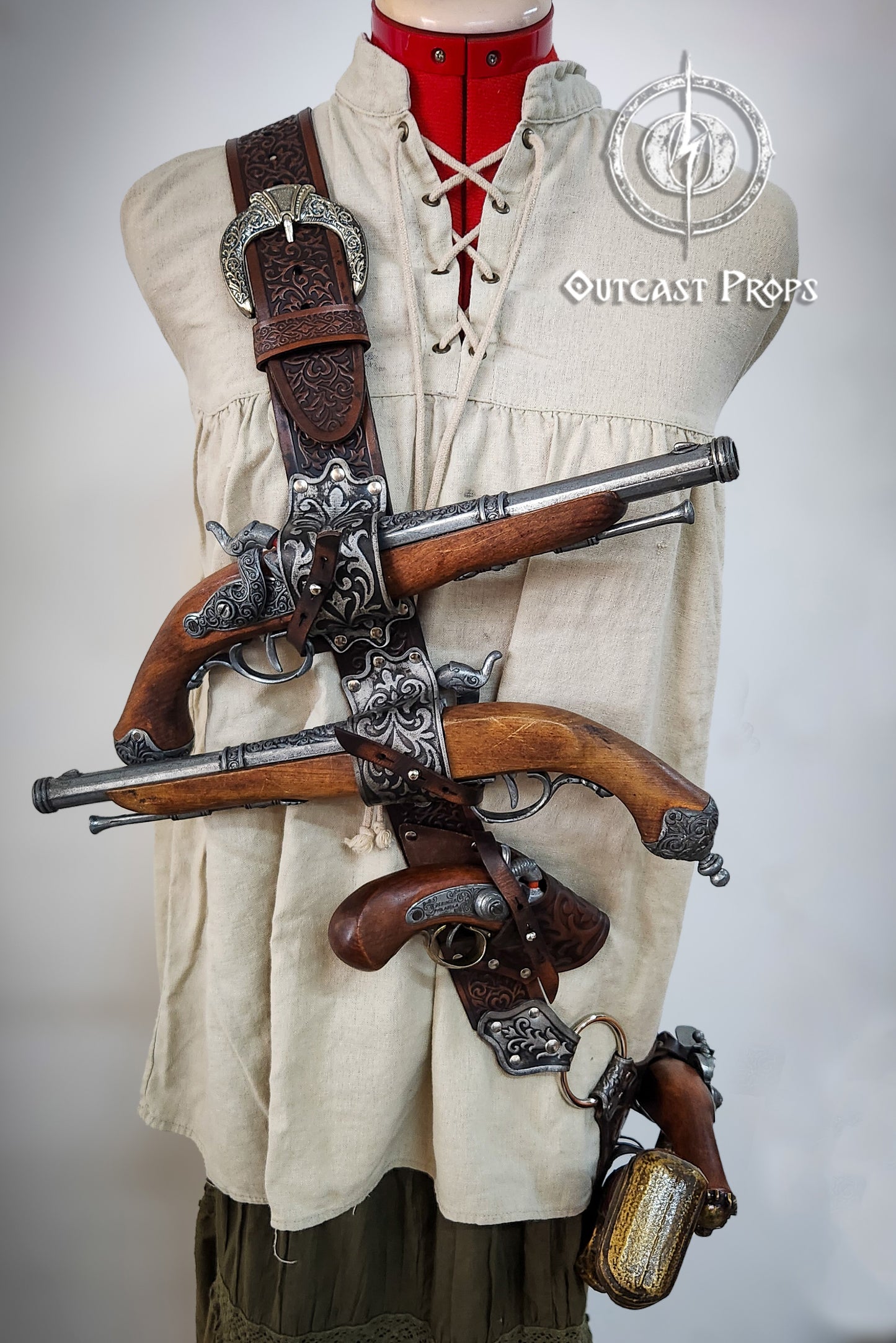 Mannequin wearing a historical outfit with a crossbow and pistols, branded 'Outcast Props'. Pirate baldric for 4 flintlock pistols and a sword, inspired by Blackbeard, Anne Bonny, Captain Kidd and Pirates of the Caribbean. Ideal for LARP, Renfaire, renaissance fair, Pirate Weekend, cosplay, Halloween and Black Sails. Silver-engraved leather, handmade with vegetable-tanned leather. Premium pirate shoulder belt for Jack Sparrow costume, historical reenactment and fantasy events. High quality pirate accessory