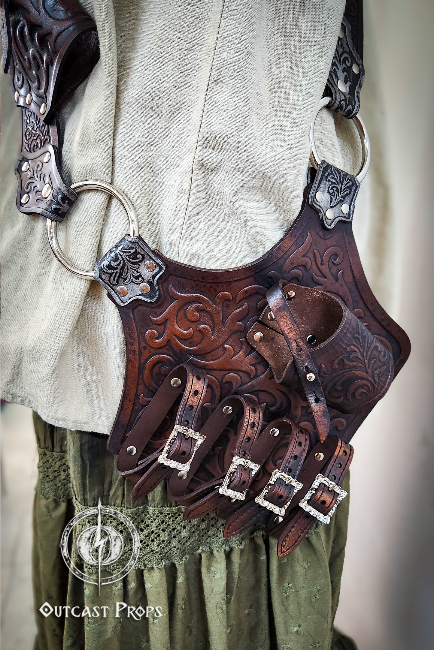 Decorative leather belt with intricate designs worn over a light-colored shirt and green pants. Pirate baldric for 4 flintlock pistols and a sword, inspired by Blackbeard, Anne Bonny, Captain Kidd and Pirates of the Caribbean. Ideal for LARP, Renfaire, renaissance fair, Pirate Weekend, cosplay, Halloween and Black Sails. Silver-engraved leather, handmade with vegetable-tanned leather. Premium pirate shoulder belt for Jack Sparrow costume, historical reenactment and fantasy events. High quality pirate access