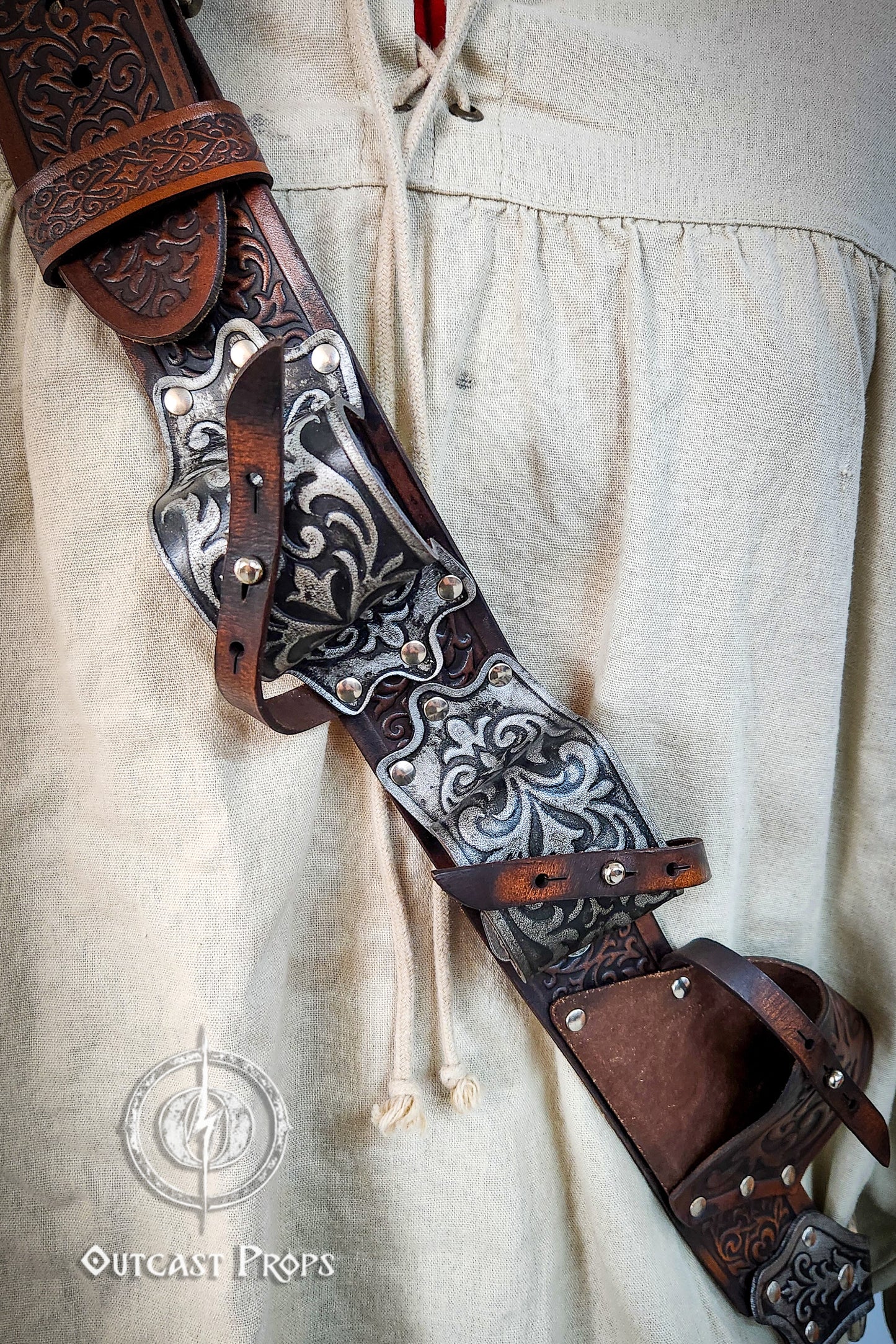 Decorative leather belt with intricate patterns on a light fabric background. Pirate baldric for 4 flintlock pistols and a sword, inspired by Blackbeard, Anne Bonny, Captain Kidd and Pirates of the Caribbean. Ideal for LARP, Renfaire, renaissance fair, Pirate Weekend, cosplay, Halloween and Black Sails. Silver-engraved leather, handmade with vegetable-tanned leather. Premium pirate shoulder belt for Jack Sparrow costume, historical reenactment and fantasy events. High quality pirate accessory for themed out