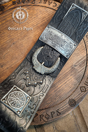 Decorative belt with intricate designs on a wooden surface, featuring the brand 'Outcast Props'. Detailed view of crescent-shaped silver buckle and engraved plates on black leather. This persian leather belt combines historical elegance and sturdy design. Crafted for LARP belt for costume and fantasy outfits.