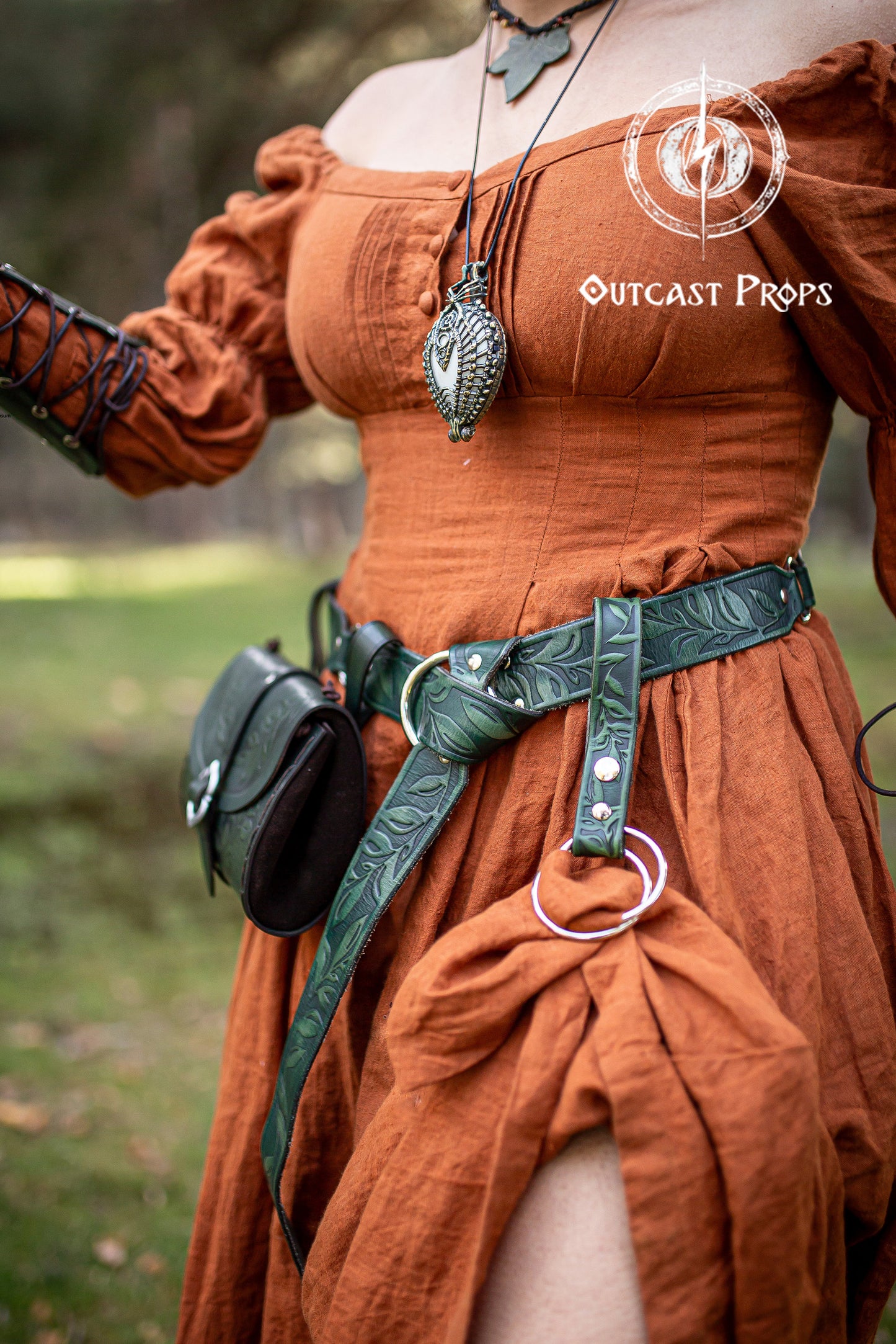 Green floral leather belt set with matching hip pouch and skirt hikes, styled with a rust-orange medieval dress. Perfect for fantasy roleplay, LARP, Ren Faires, or cosplay events. Handmade and hand-dyed using vegetable tanning techniques, offering an elegant and durable accessory to carry essentials during adventures or magical gatherings.