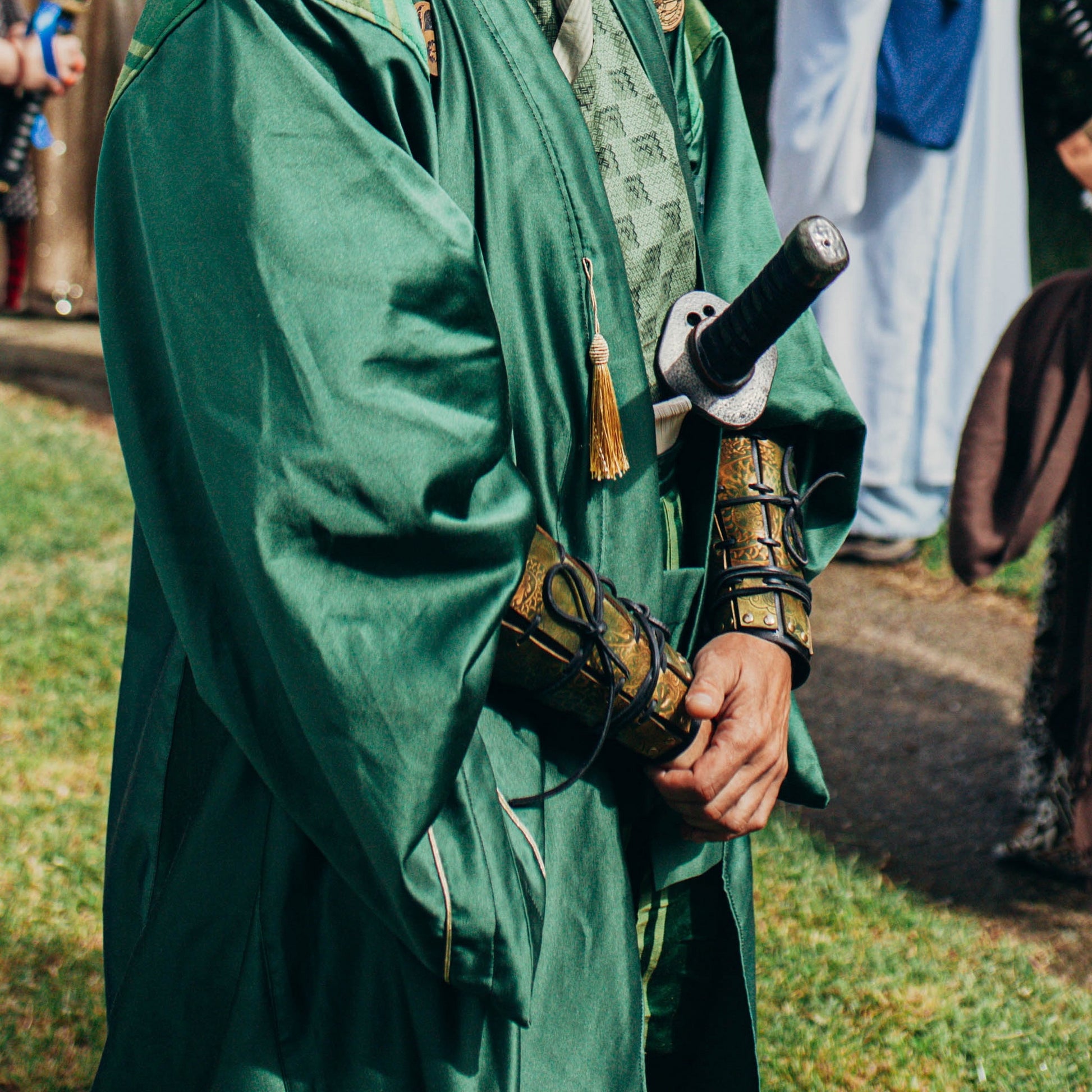 Detail shot of green robe and samurai cosplay armor showing golden engraved dragon bracers. Ideal for fantasy larp, samurai costume, or Asian-inspired RPG outfits. Bracers handcrafted in leather with vegetable dyes and precise engraving. Lightweight yet bold, suitable for long wear in immersive events. Aged with care using Outcast Props’ unique techniques. Not real armor, costume use only.