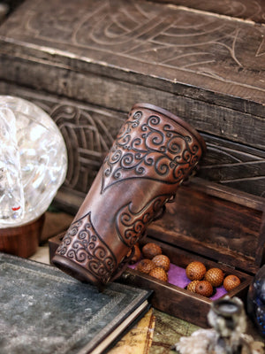 A pair of brown leather bracers with intricate embossed patterns, displayed on a surface with a mirror and a crystal ball. Shadowbinder bracer for mages & wizards, sorcerer vambarce for larp costume and wizardry cosplay leather witchcraft handmade