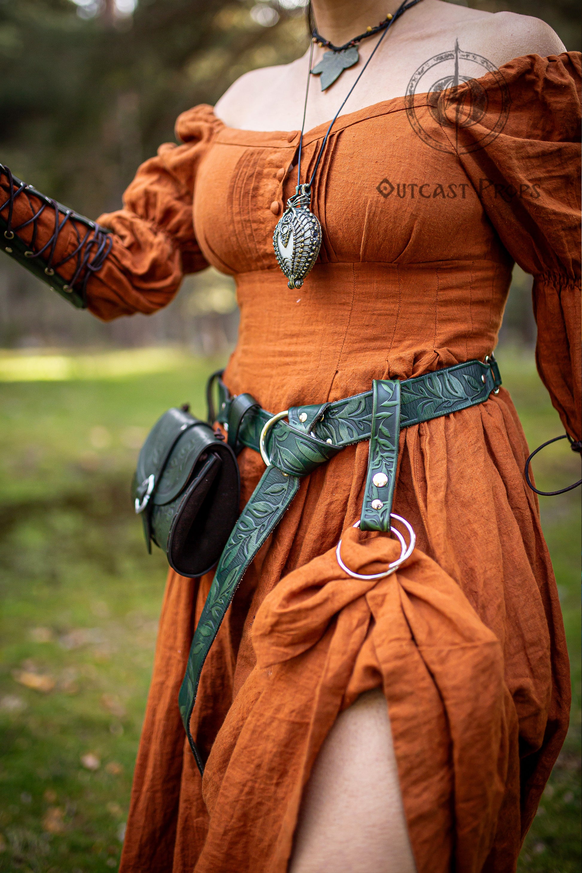 A green leather belt with floral designs and silver accents. The belt is worn over a rust-colored dress. The belt has a silver ring attached to it. Medieval Floral Leather Skirt Hike Ring LARP Ren Faire Cosplay Accessory for Fantasy Outfits Skirt Hiker Renaissance Fair Costume Accessory