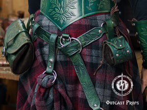 A green version of the floral leather skirt hike is shown clipped to a belt over a thick plaid wool skirt, paired with matching green tooled leather armor and pouches. The embossed leaf pattern, double O-ring system and snap closure allow the wearer to gather fabric and secure it for movement or style. Ideal for LARP, Renaissance faire and fantasy costumes, the accessory adds charm while supporting pouches, tankards or potion holders as part of an immersive character outfit.