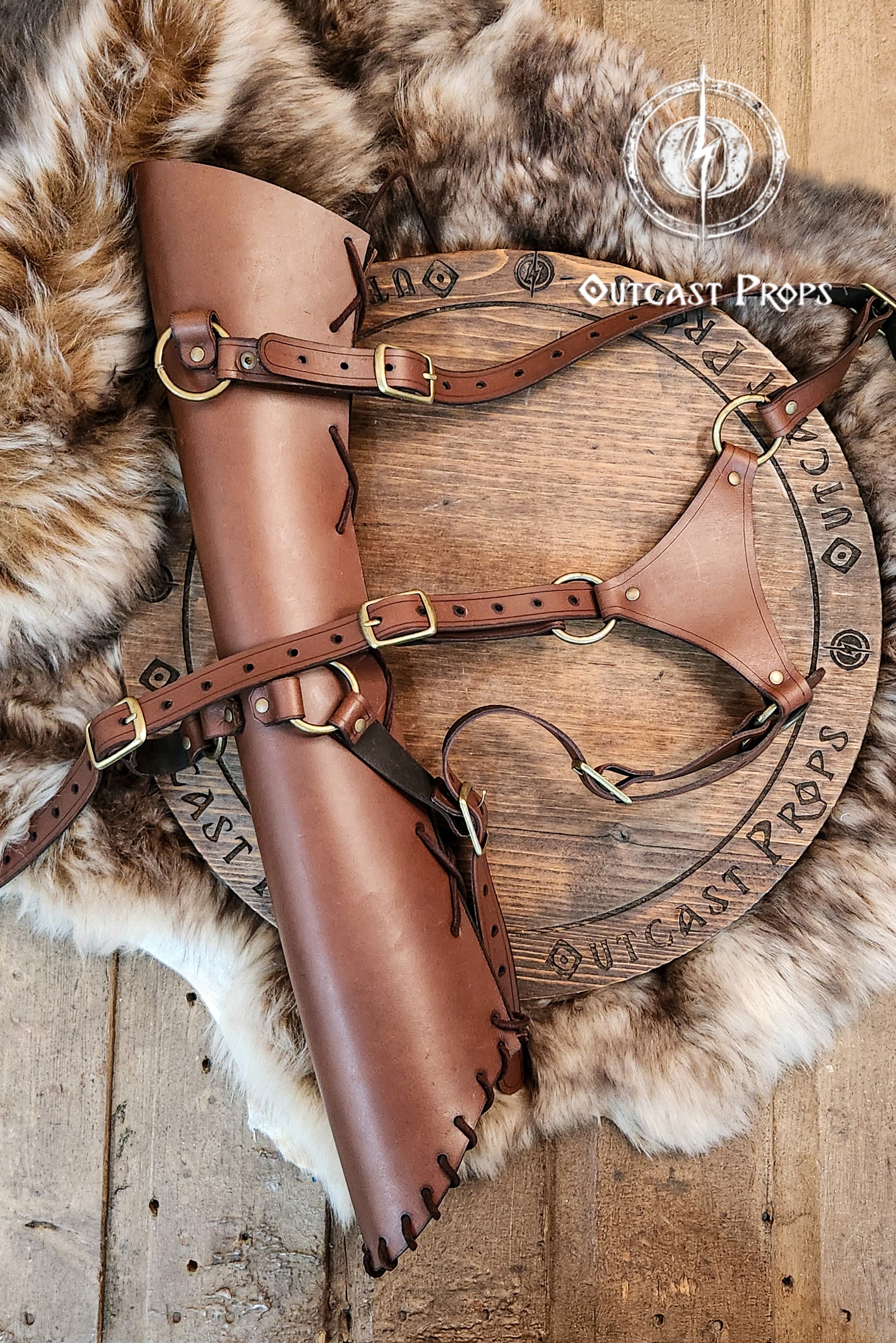 Close-up of a handcrafted leather quiver with full adjustable harness, resting on a wooden disc with fur in the background. The brown leather and brass buckles showcase the artisan quality. Ideal for archery quiver setups, larp quiver wear, cosplay, or medieval reenactment. A beautiful choice for fans of leather quiver and bow and arrow props. Durable, stylish and fantasy-ready.