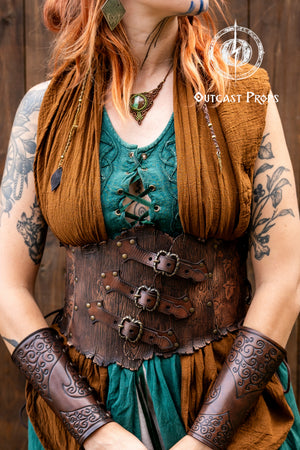 Person in a fantasy costume with 'Outcast Props' logo in the corner. Person wearing a detailed leather corset with decorative elements, branded 'Outcast Props'. Underbust Wood Leather Corset. Herbalist corset. Druid corset. Elven Corset. Ivy Corset.