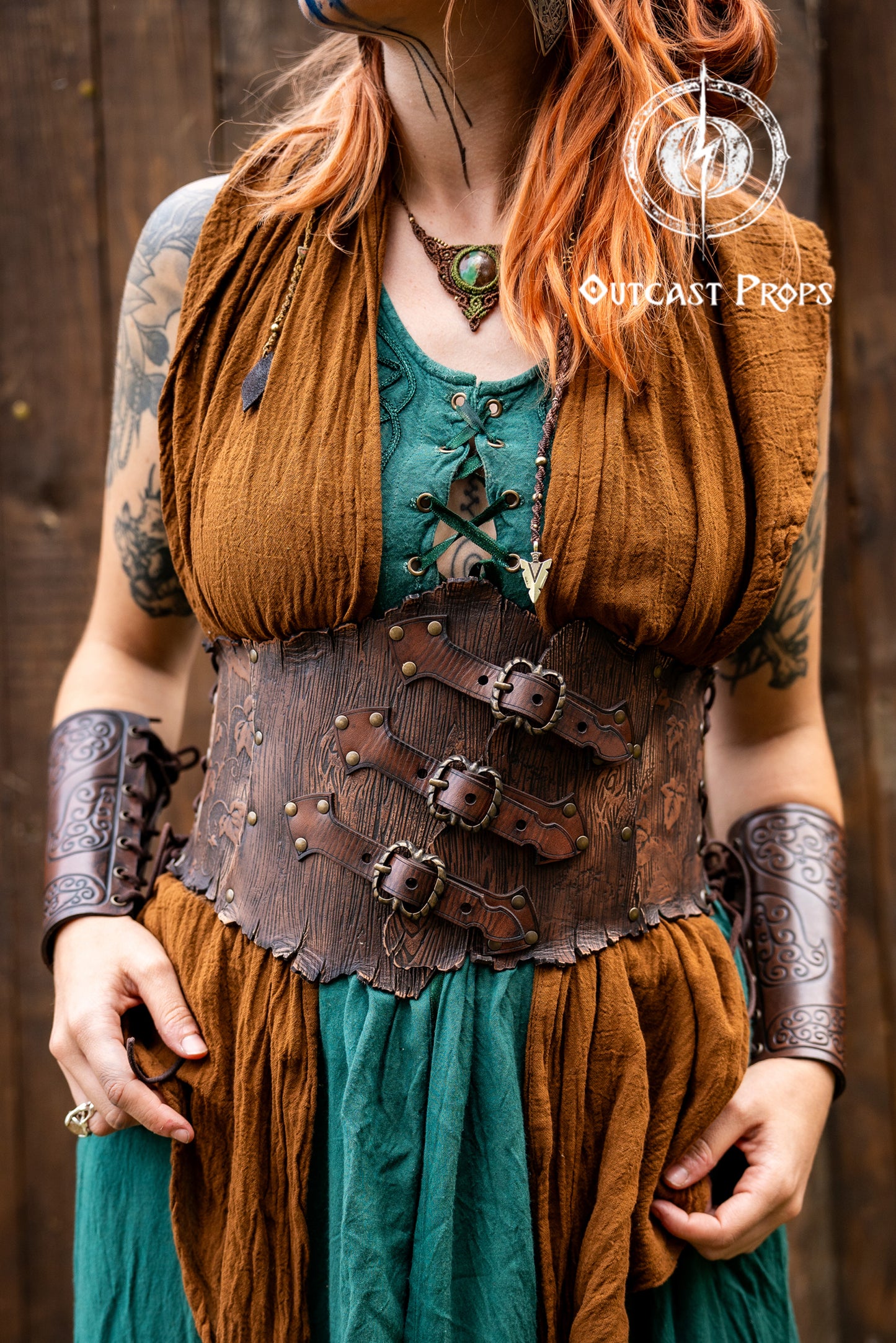 Person in a fantasy costume with 'Outcast Props' logo in the corner. Person wearing a detailed leather corset with decorative elements, branded 'Outcast Props'. Underbust Wood Leather Corset. Herbalist corset. Druid corset. Elven Corset. Ivy Corset.