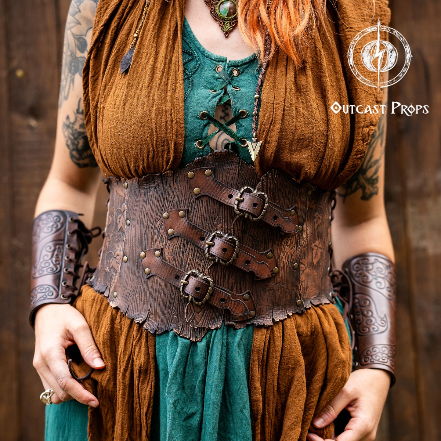 Person in a fantasy costume with 'Outcast Props' logo in the corner. Person wearing a detailed leather corset with decorative elements, branded 'Outcast Props'. Underbust Wood Leather Corset. Herbalist corset. Druid corset. Elven Corset. Ivy Corset.