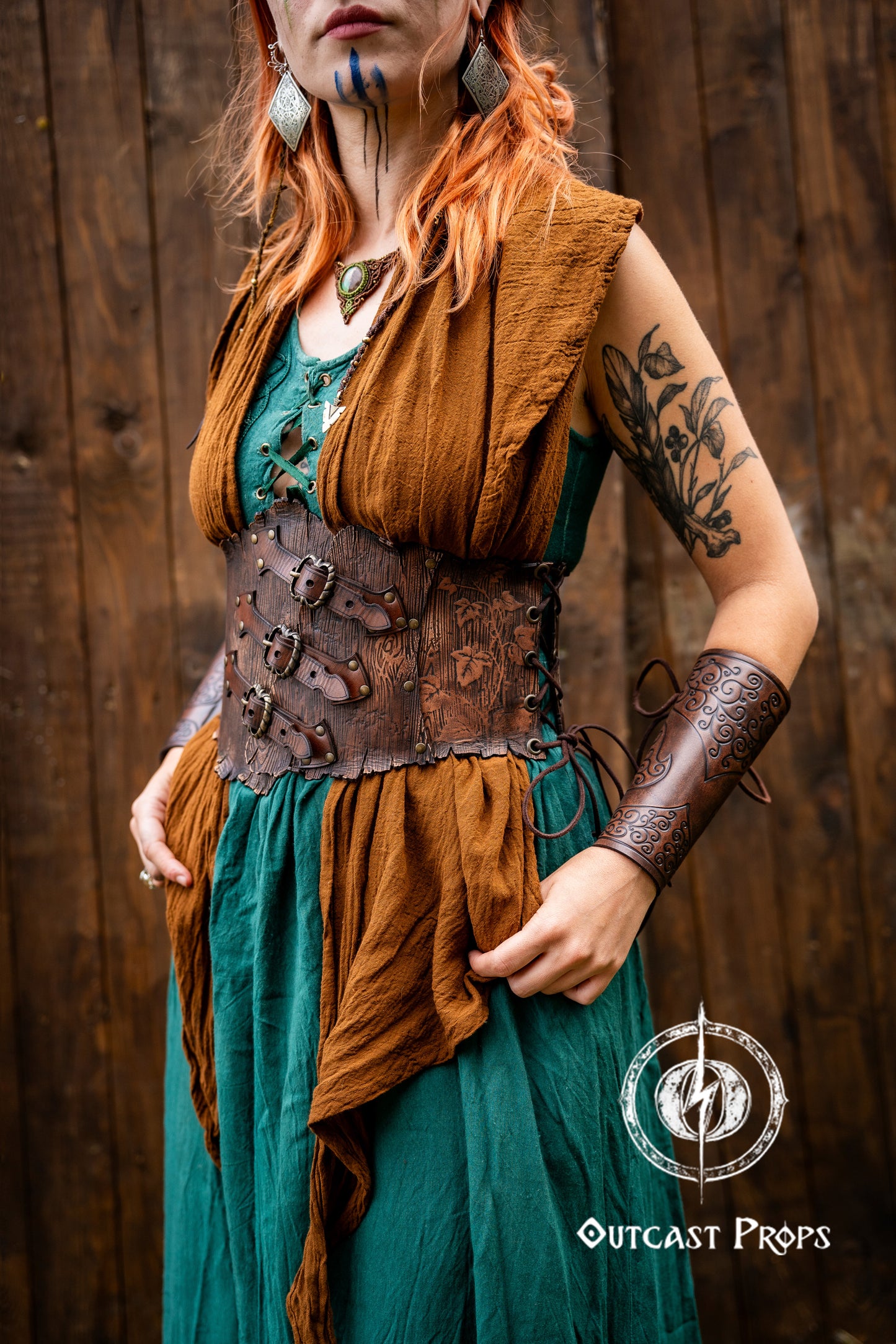 Person in a fantasy costume with 'Outcast Props' logo in the corner. Person wearing a detailed leather corset with decorative elements, branded 'Outcast Props'. Underbust Wood Leather Corset. Herbalist corset. Druid corset. Elven Corset. Ivy Corset.