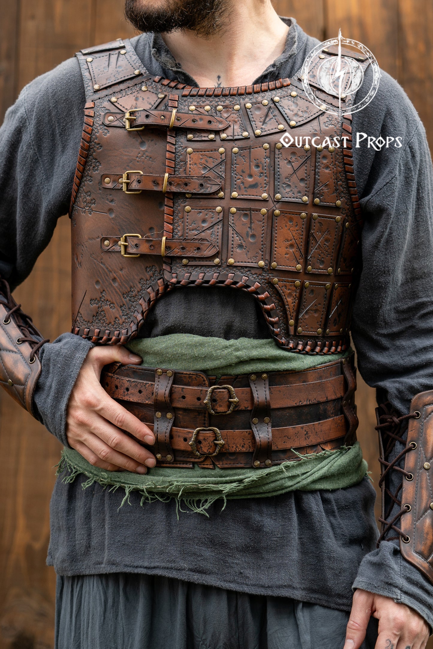 Person wearing a detailed leather armor vest with 'Outcast Props' branding. Close-up of a detailed costume with leather straps and a green cloth, branded 'Outcast Props'. Veteran Leather Belt premium vegetable-tanned, worn by raiders and mercenaries.
