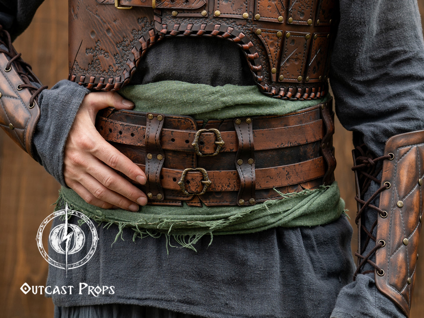 Person wearing a detailed leather armor vest with visible Outcast Props. Close-up of a detailed costume with leather straps and a green cloth, branded 'Outcast Props'. Veteran Leather Belt premium vegetable-tanned, worn by raiders and mercenaries.branding.