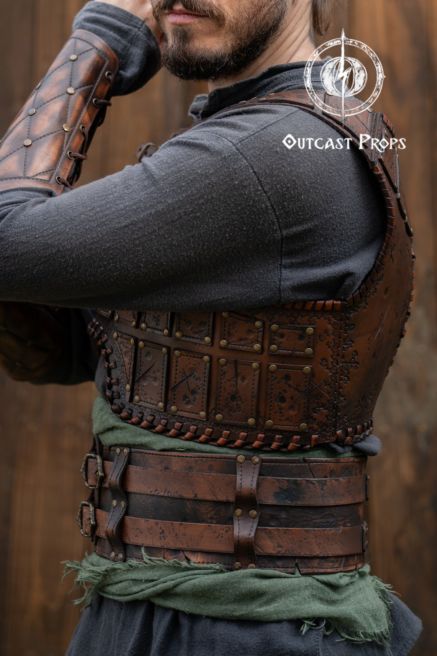 Person wearing a detailed leather armor vest with 'Outcast Props' branding. Close-up of a detailed costume with leather straps and a green cloth, branded 'Outcast Props'. Veteran Leather Belt premium vegetable-tanned, worn by raiders and mercenaries.