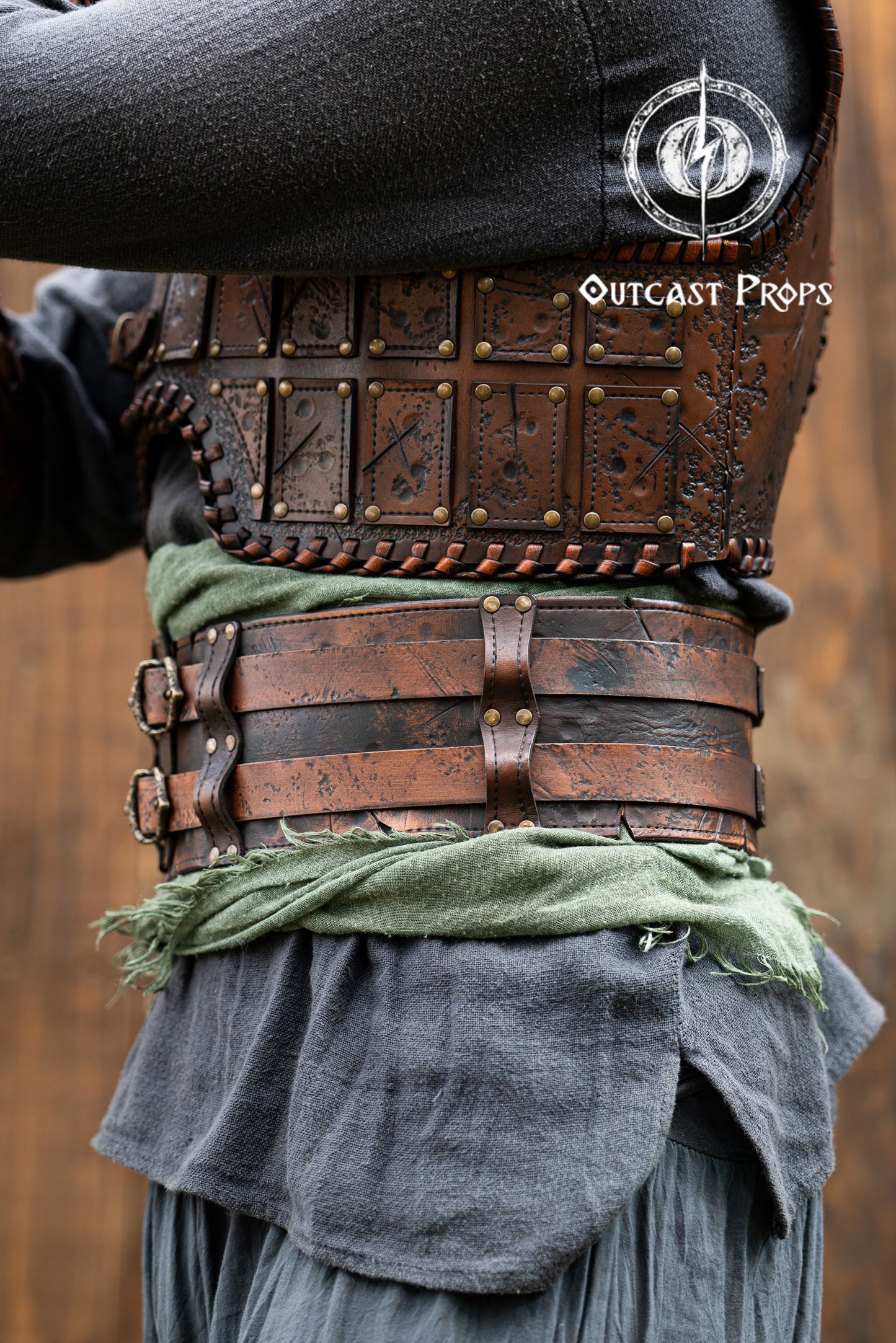 Close-up of a detailed costume with leather straps and a green cloth, branded 'Outcast Props'. Veteran Leather Belt premium vegetable-tanned, worn by raiders and mercenaries.
