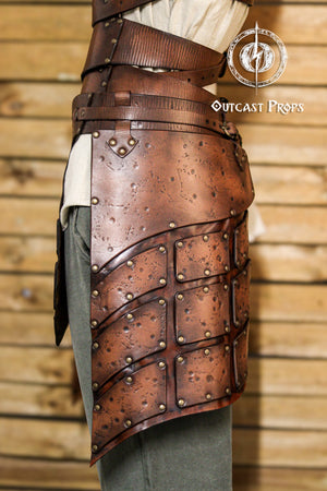 Close-up side view of brown leather tassets with brass rivets and distressed finish. Perfect for female warrior costumes, this handcrafted element of a LARP armor set provides protection and mobility for fantasy, viking or ranger characters.