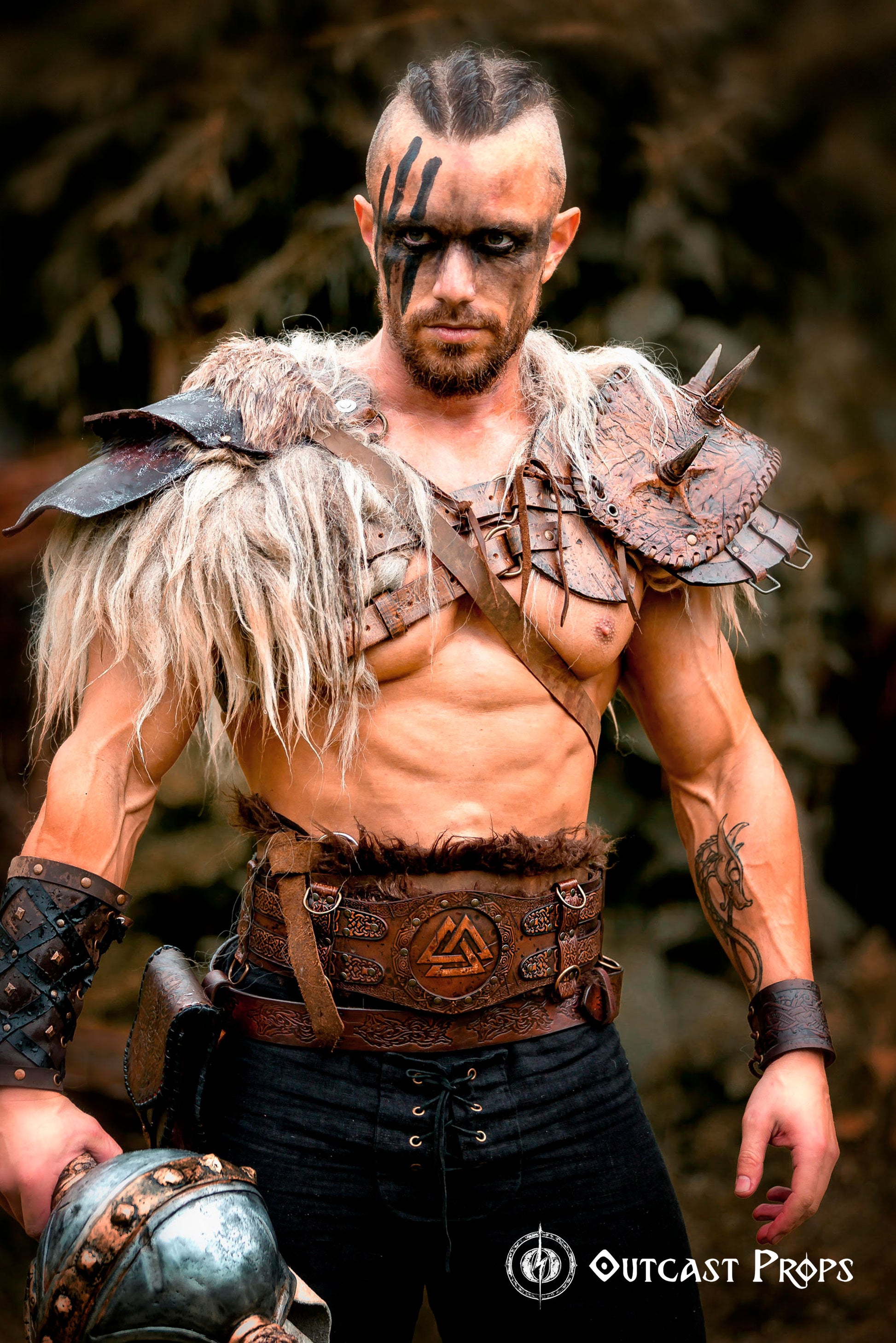 Viking leather armor belt with Valknut engraving worn by a male model in fur shoulder armor. Perfect for barbarian cosplay outfit, celtic fantasy belt, or medieval warrior armor. The embossed wide belt features decorative rivets and a central symbol, set in a rustic Viking hut. Ideal for LARP, renfaire costume wide, or fantasy events.
