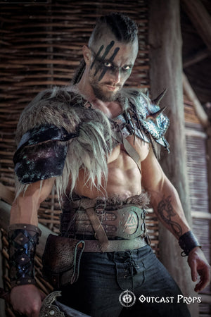 Barbarian cosplay outfit worn by a male model showing the viking leather armor belt with Valknut design. The wide belt cinches the waist and supports pouches and gear, matching the celtic fantasy belt theme. Ideal for LARP, fantasy warrior look, or renfaire costume. The photo captures the rugged, immersive style in a dark wooden hut.