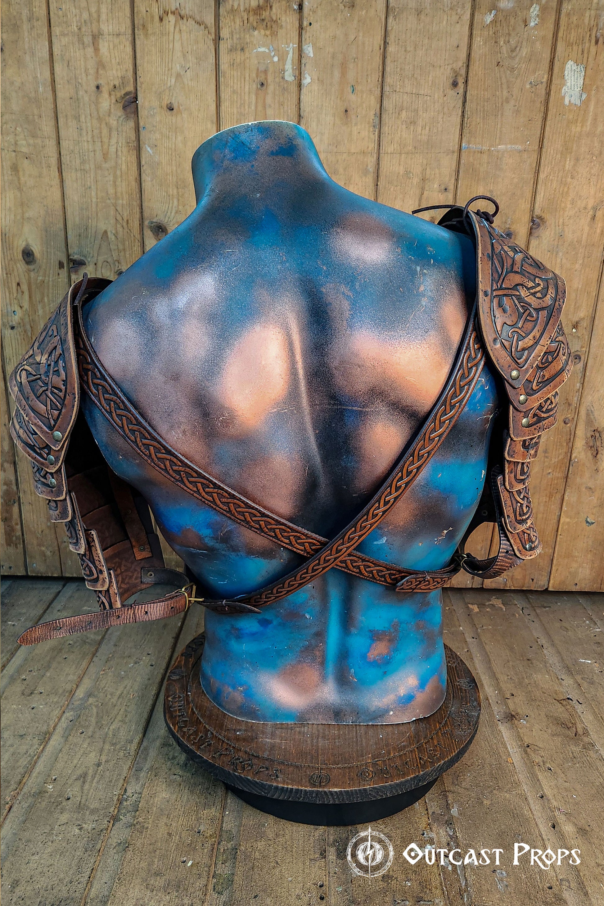 Rear view of Viking leather shoulder armor Sedrik, showcasing adjustable leather straps crossed on the back of a sculpted mannequin torso. Detailed engraved Celtic patterns on leather pauldrons visible from both sides. Rustic wooden background enhances the handcrafted leather's aged aesthetic. Ideal for Norse cosplay, Celtic warrior costume, Viking LARP gear, fantasy armor set, medieval reenactment outfit, premium leather shoulder armor.