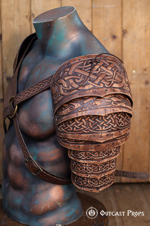 Side profile of Sedrik Viking leather shoulder armor in brown full-grain leather with deep engraved Celtic knot patterns. Layered construction for flexible movement, shown on an anatomically sculpted mannequin torso with crossed leather straps and rustic wood backdrop. Perfect for Viking cosplay, Celtic LARP armor, Norse warrior outfit, fantasy and medieval costume gear, premium handcrafted leather pauldrons for immersive roleplay events.