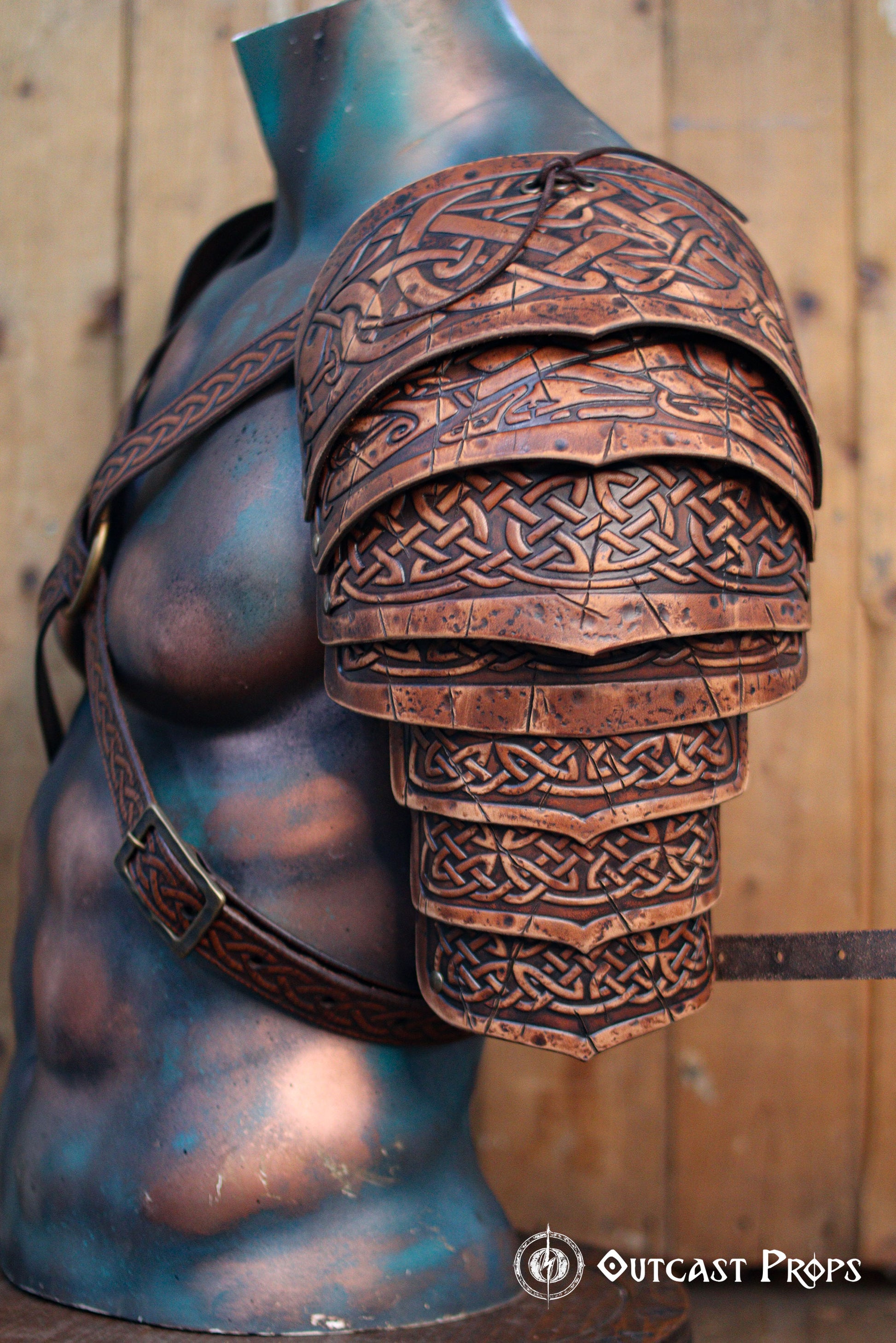Detailed side view of Sedrik Viking leather shoulder armor, showing layered brown leather plates engraved with Celtic knotwork and aged patina. Armor worn on a sculpted mannequin torso with embossed leather straps crossing the chest. Rustic wooden backdrop complements the handcrafted finish. Perfect for Viking warrior cosplay, Celtic LARP armor, Norse costume gear, fantasy medieval reenactment outfit, premium leather shoulder pauldrons.
