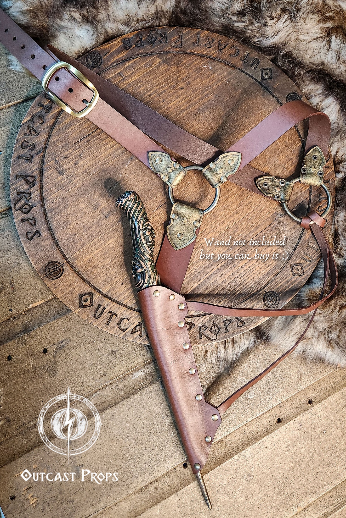 A brown leather wand holster with dual metal rings and riveted construction. Styled for Voldemort-inspired cosplay or LARP magic duels. Crafted for comfort and realism in wizard costumes, especially for Harry Potter fans recreating Death Eater aesthetics.Magic-style leather belt with decorative elements on a wooden surface, featuring Outcast Props branding.