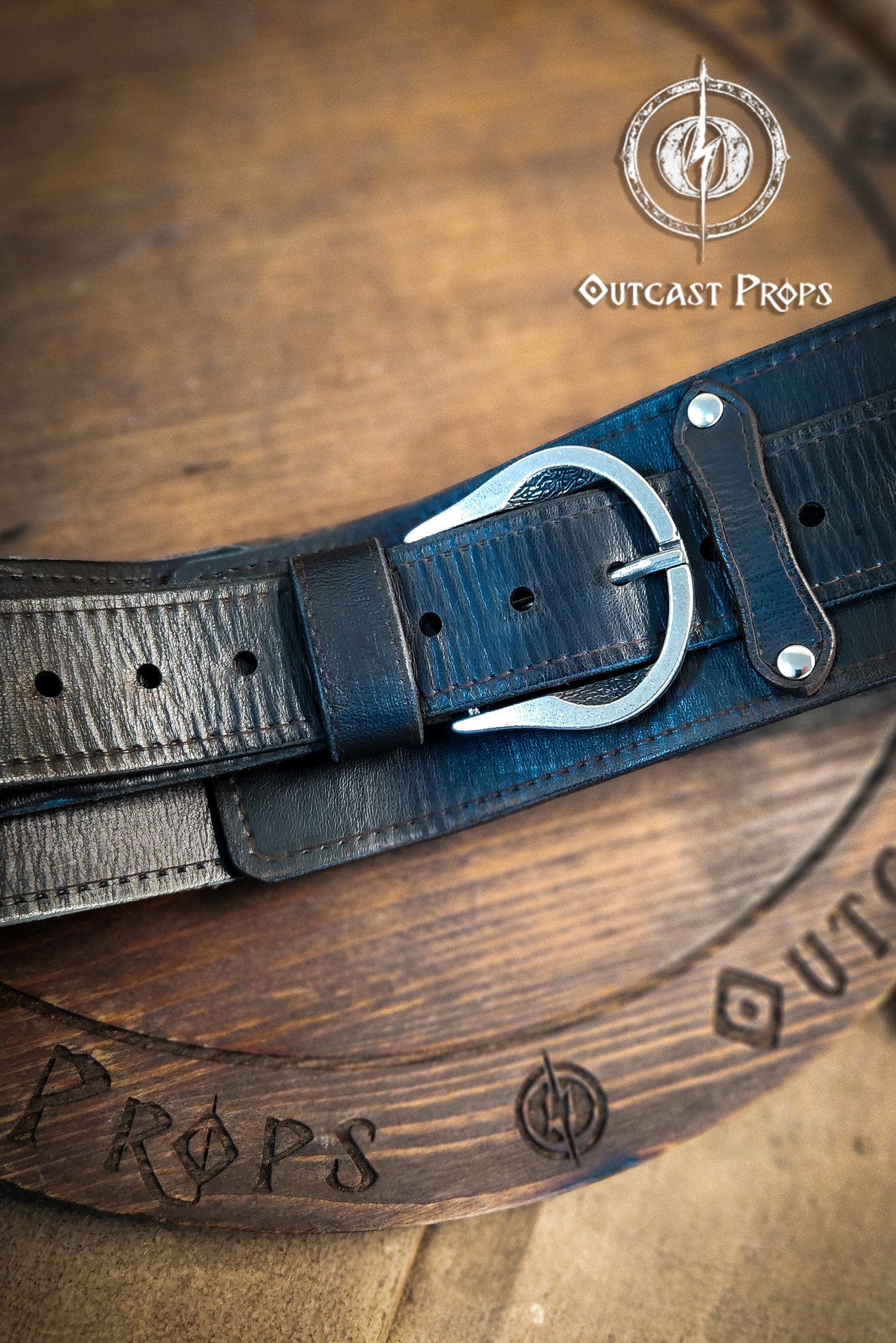 Black leather belt with brass buckle on a wooden surface, branded 'Outcast Props'. Medieval broadbelt for larp or cosplay. Elegant leather belt.