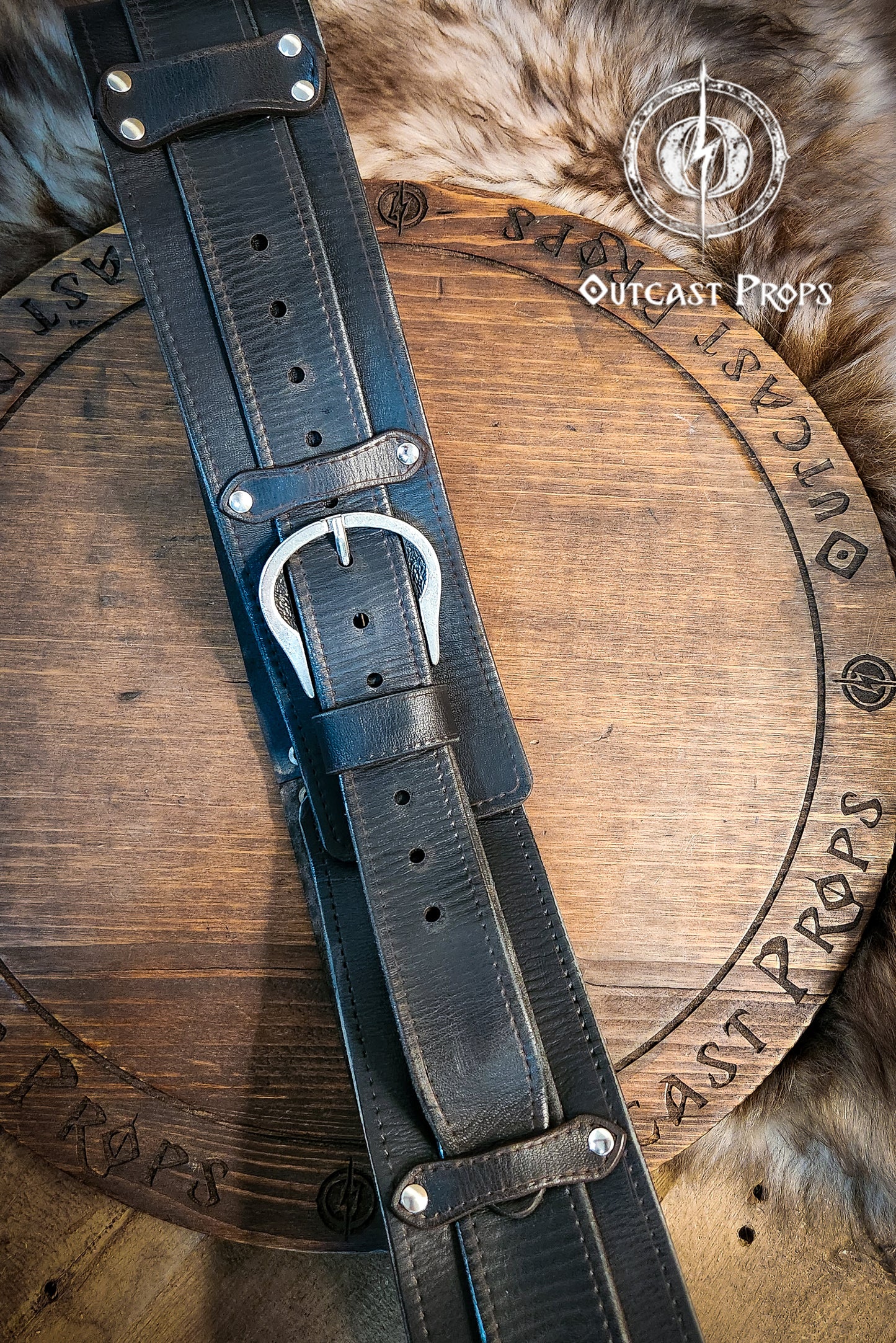 Black leather belt with brass buckle on a wooden surface, branded 'Outcast Props'. Medieval broadbelt for larp or cosplay. Elegant leather belt.