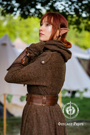 Person wearing a brown coat with a belt, standing outdoors with blurred tents in the background. Celtic knot leather belt silver buckle larp belt for ren fair fantasy costume celtic belt unisex leather belt for renaissance outfit