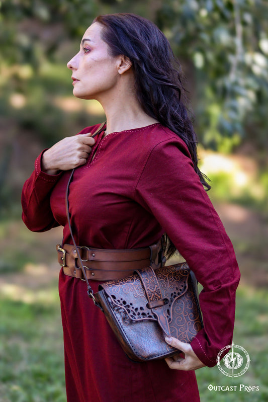 A person in a red dress is wearing a brown leather bag with intricate embossed designs, across their body.