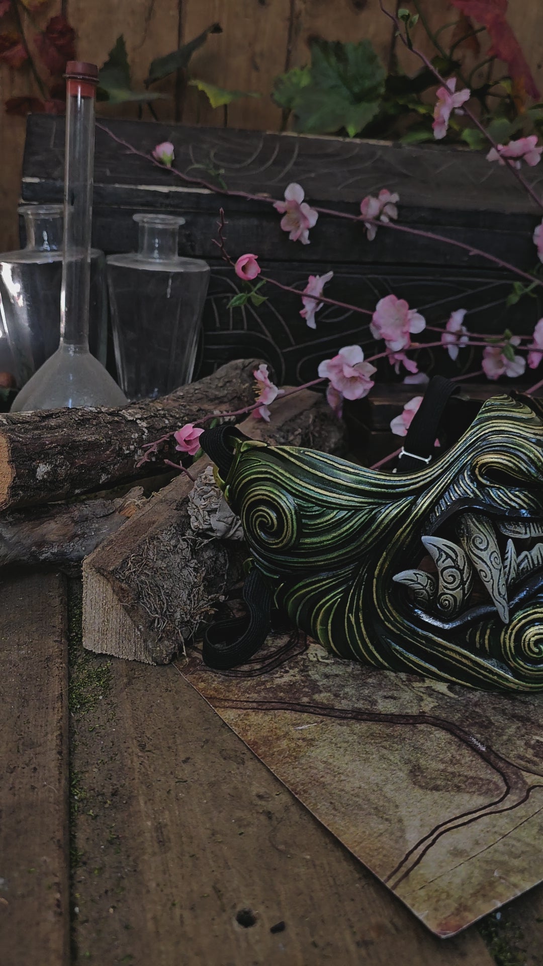 A hand-painted Oni Samurai Mempo mask with red and black details, displayed on a surface with a map background and pink flowers in the peripheral. Samurai oni mask japanese half oni mask samurai wearable mask for cosplay larp menpo mask scorpion clan mask l5r samurai mask