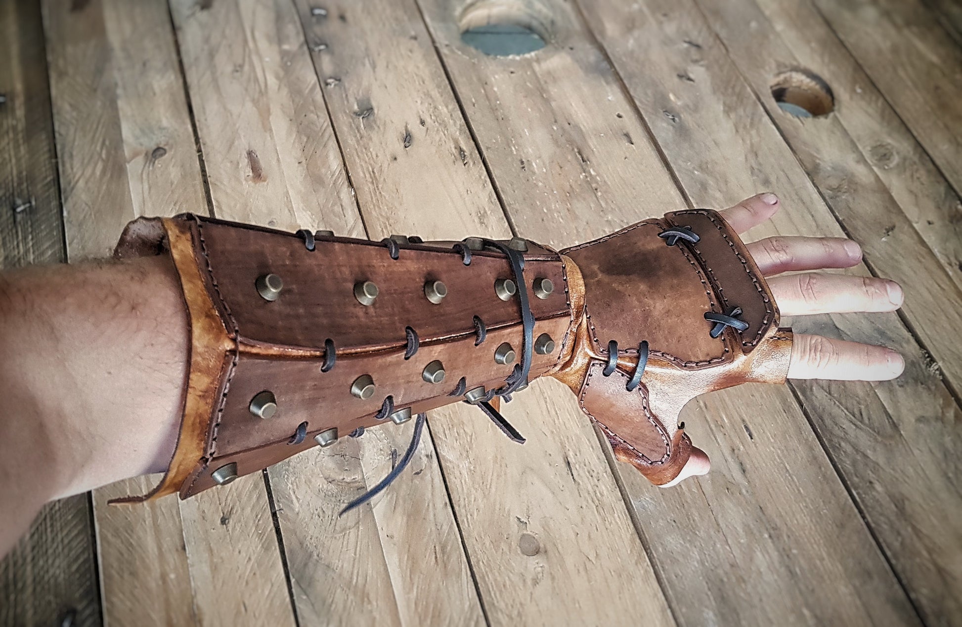 A person's forearm wearing a brown leather bracer with metal rivets and buckles, designed for cosplay. Samurai Leather bracers, larp or cosplay leather and metal pair of bracers for fantasy cosplay, accurate replica