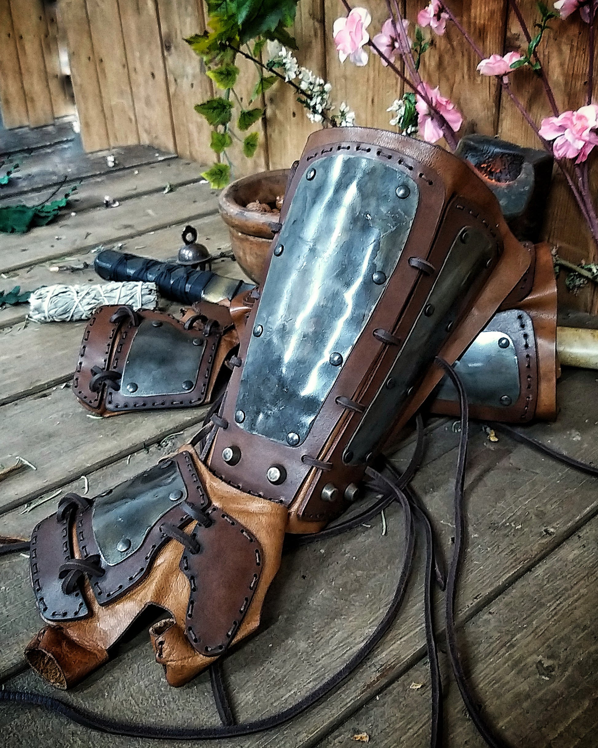 A pair of samurai armoured bracers with leather and iron components, displayed on a wooden surface with a backdrop of autumn leaves. Samurai armor iron bracers, Samurai cosplay armoured leather pair of bracers for larp, leather and Iron bracers for post apocalyptic costume
