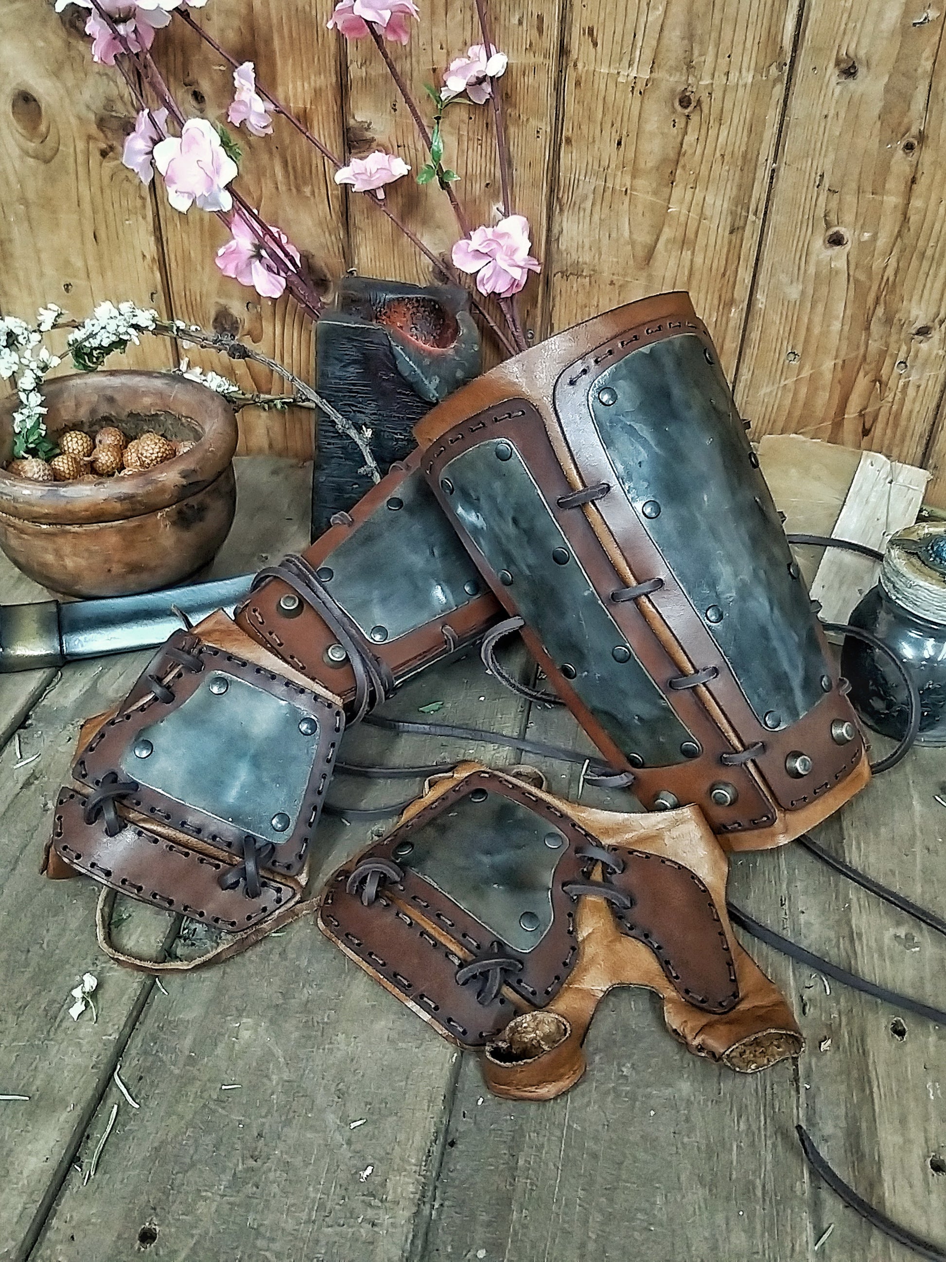 A pair of samurai armoured bracers with leather and iron components, displayed on a wooden surface with a backdrop of autumn leaves. Samurai armor iron bracers, Samurai cosplay armoured leather pair of bracers for larp, leather and Iron bracers for post apocalyptic costume