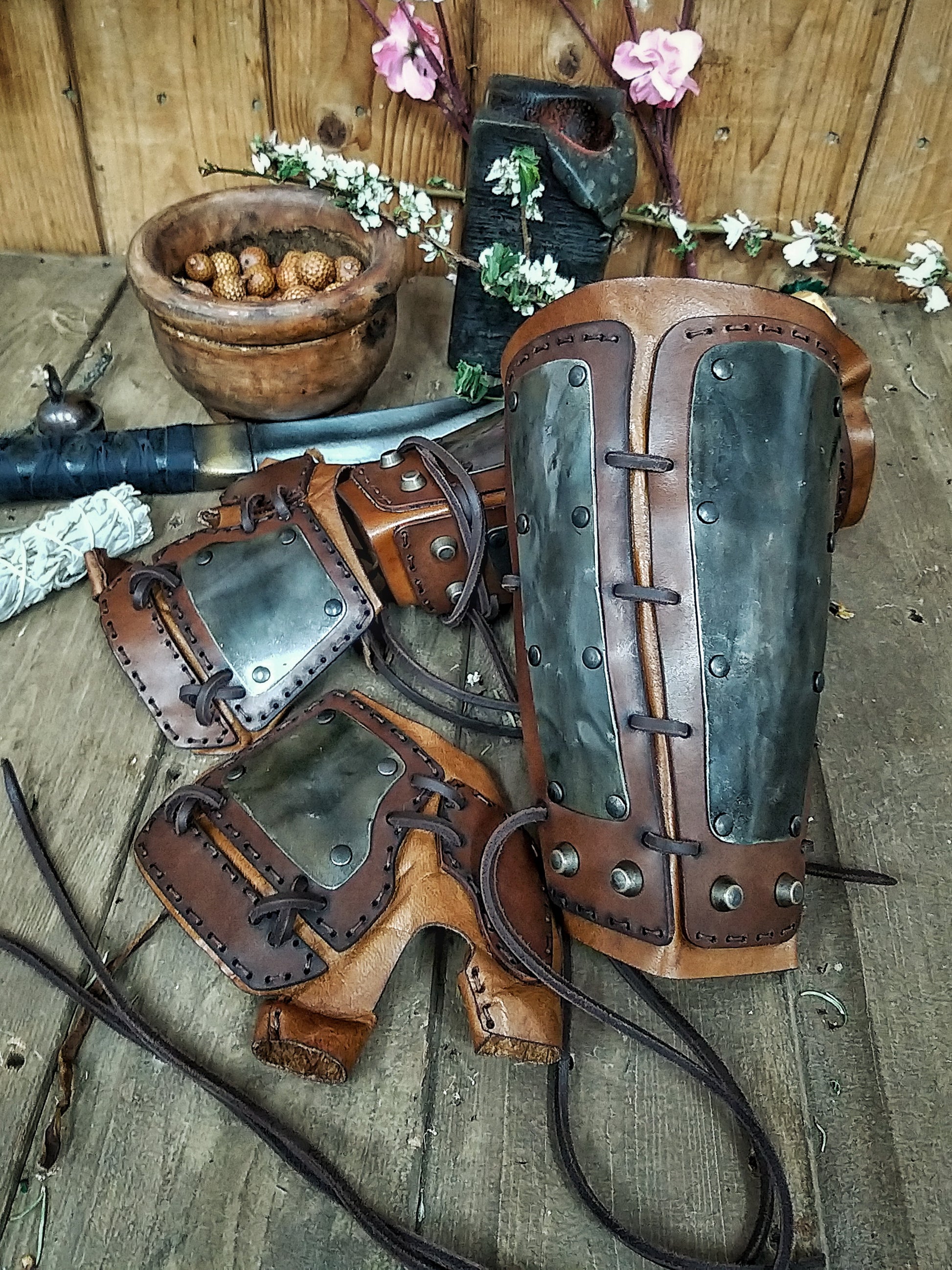 A pair of samurai armoured bracers with leather and iron components, displayed on a wooden surface with a backdrop of autumn leaves. Samurai armor iron bracers, Samurai cosplay armoured leather pair of bracers for larp, leather and Iron bracers for post apocalyptic costume