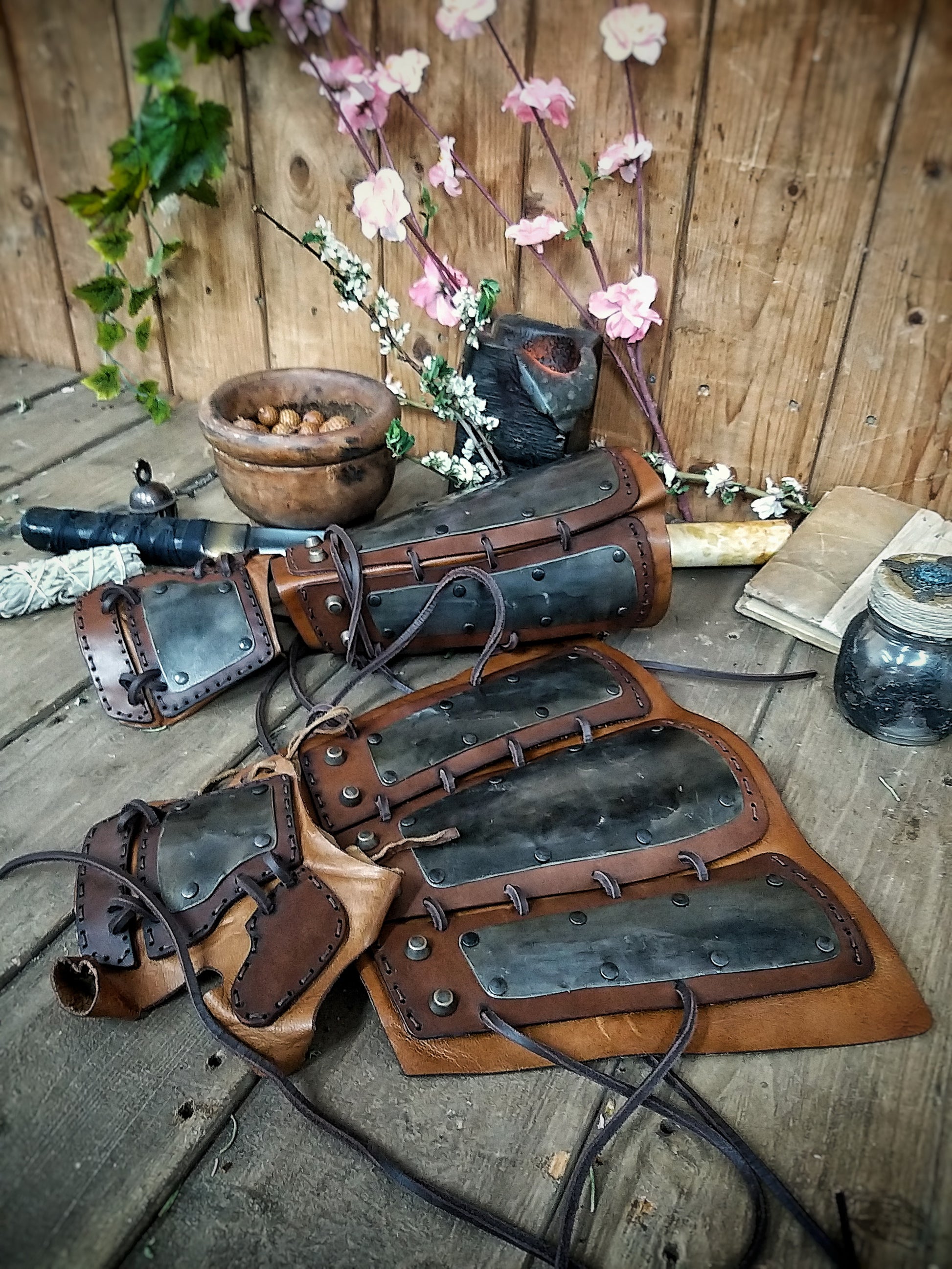 A pair of samurai armoured bracers with leather and iron components, displayed on a wooden surface with a backdrop of autumn leaves. Samurai armor iron bracers, Samurai cosplay armoured leather pair of bracers for larp, leather and Iron bracers for post apocalyptic costume