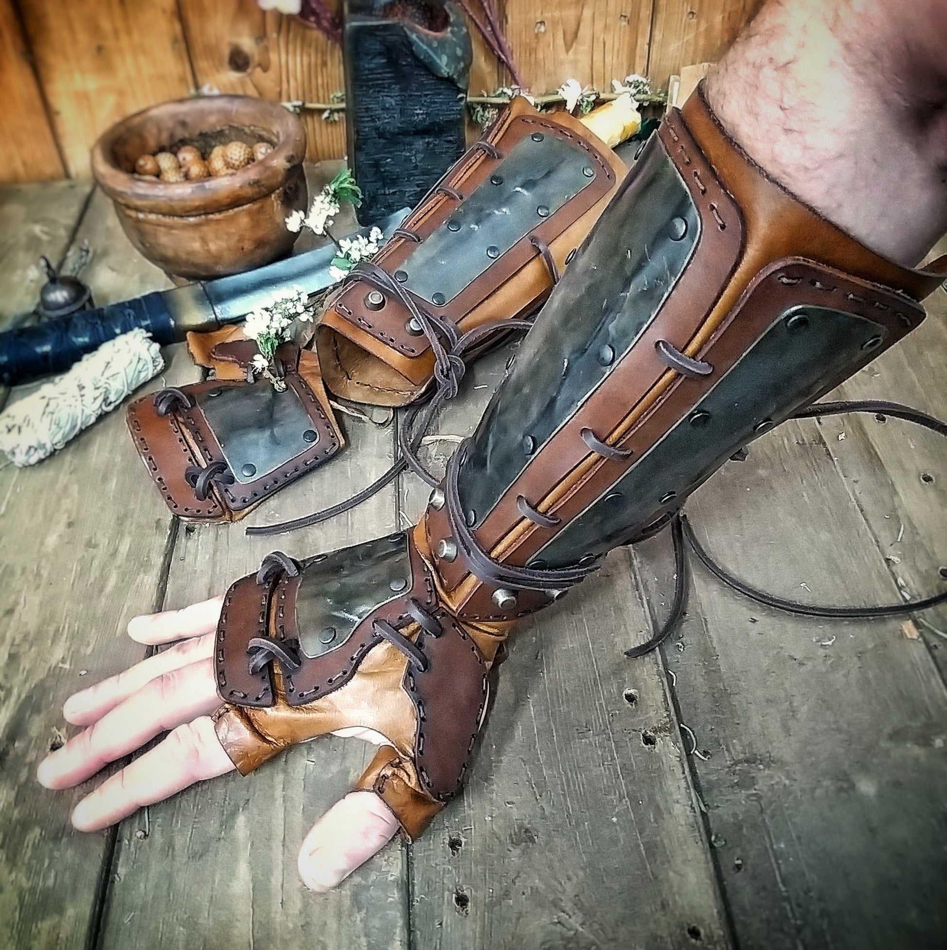 A pair of samurai armoured bracers with leather and iron components, displayed on a wooden surface with a backdrop of autumn leaves. Samurai armor iron bracers, Samurai cosplay armoured leather pair of bracers for larp, leather and Iron bracers for post apocalyptic costume