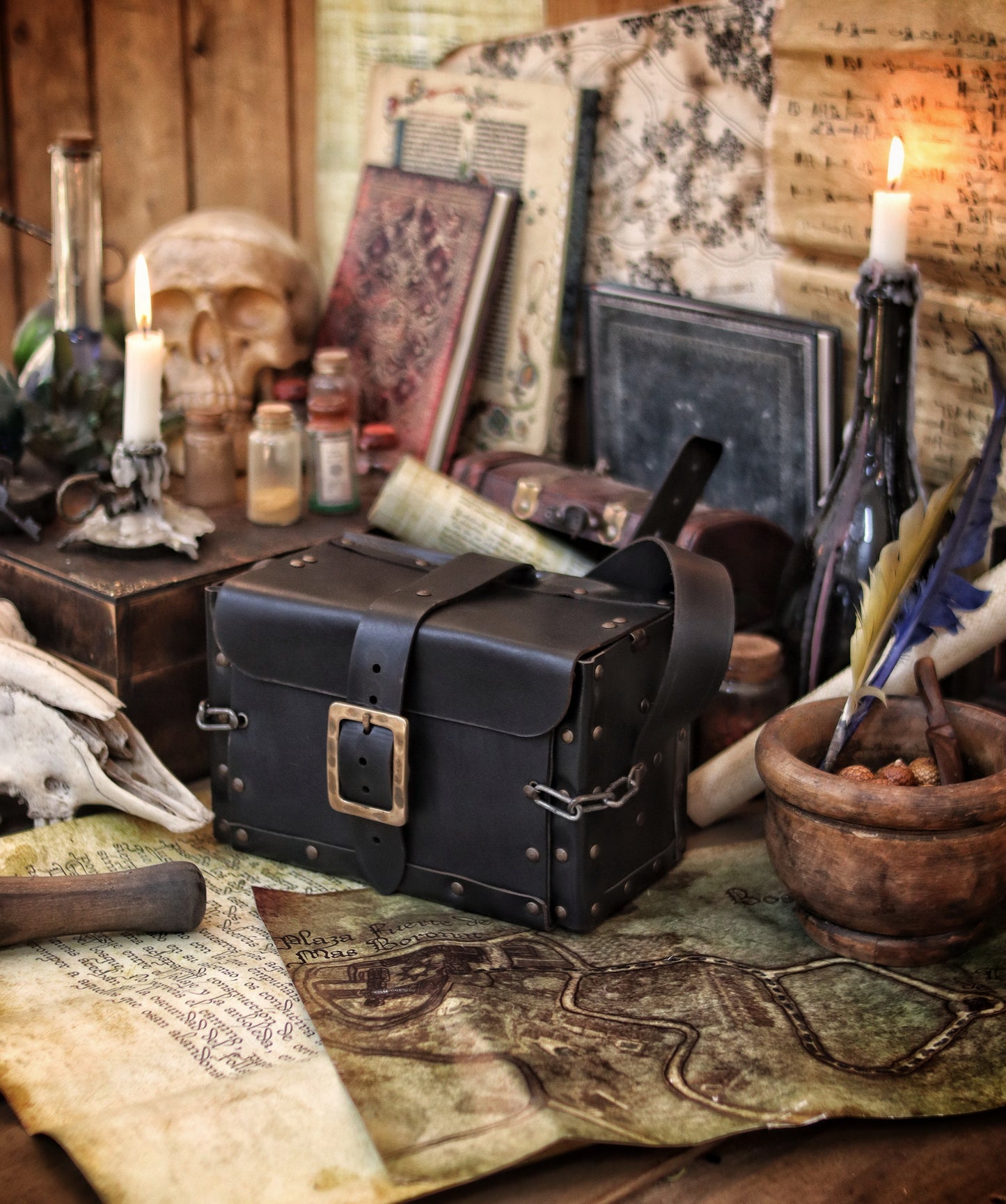 Black Alchemist Leather Bag resting on an old fantasy map, surrounded by a rustic apothecary scene with potion vials, quills, scrolls, and candles. Crafted by hand from vegetable-tanned leather, with riveted edges and a strong buckle for secure closure. Perfect for medieval, fantasy, or steampunk roleplay characters who need quick access to potions, poisons, or magical ingredients in the heat of battle.