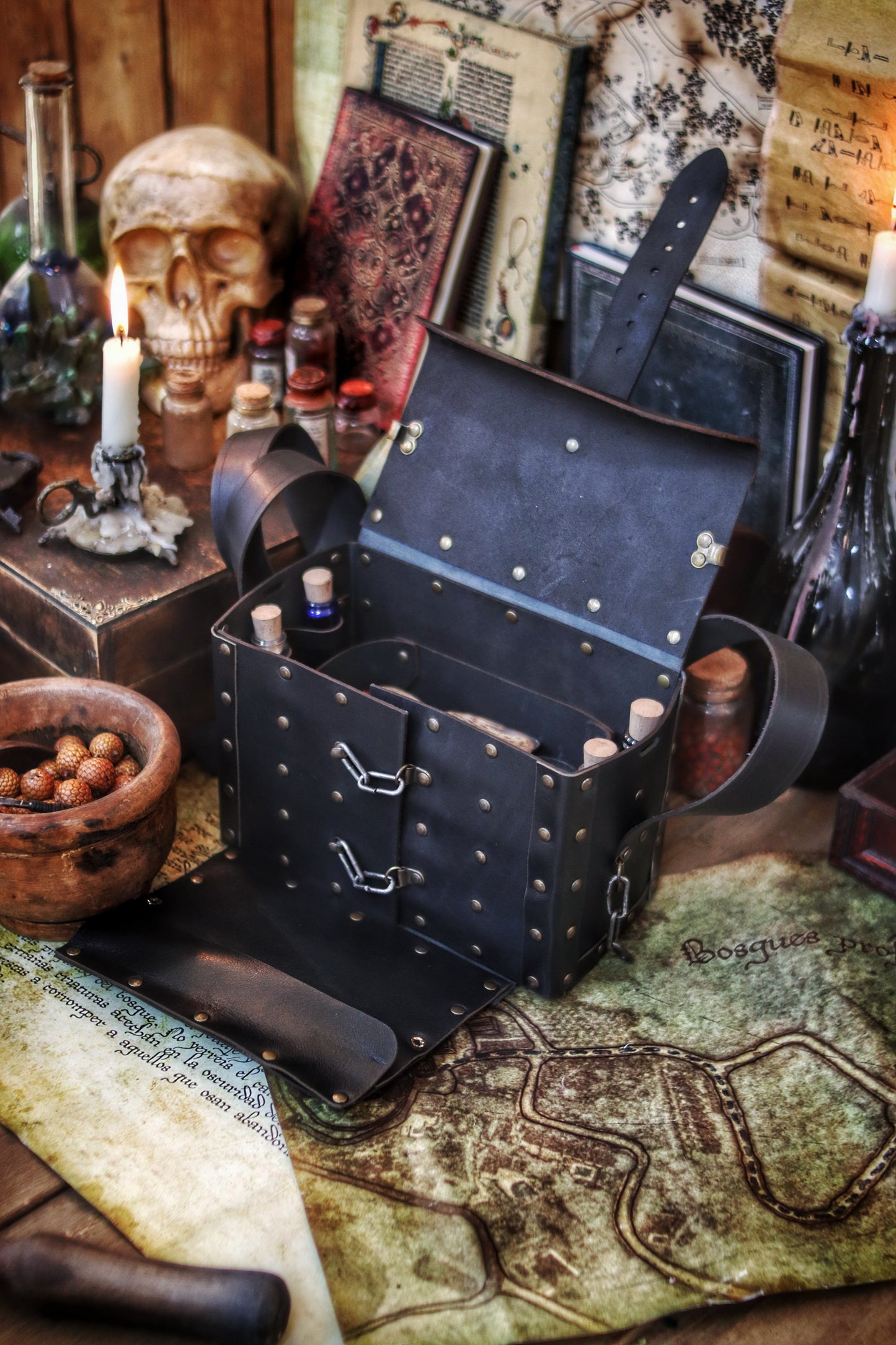 Open black Alchemist Leather Bag on a fantasy map, showing potion vials secured inside and surrounded by medieval props like scrolls, candles, and a skull. Crafted from vegetable-tanned leather with metal rivets and secure latches. Designed for LARP, cosplay, or fantasy adventures, offering quick access to potions or antidotes without fully opening the bag. A perfect companion for alchemists, healers, or wizards.