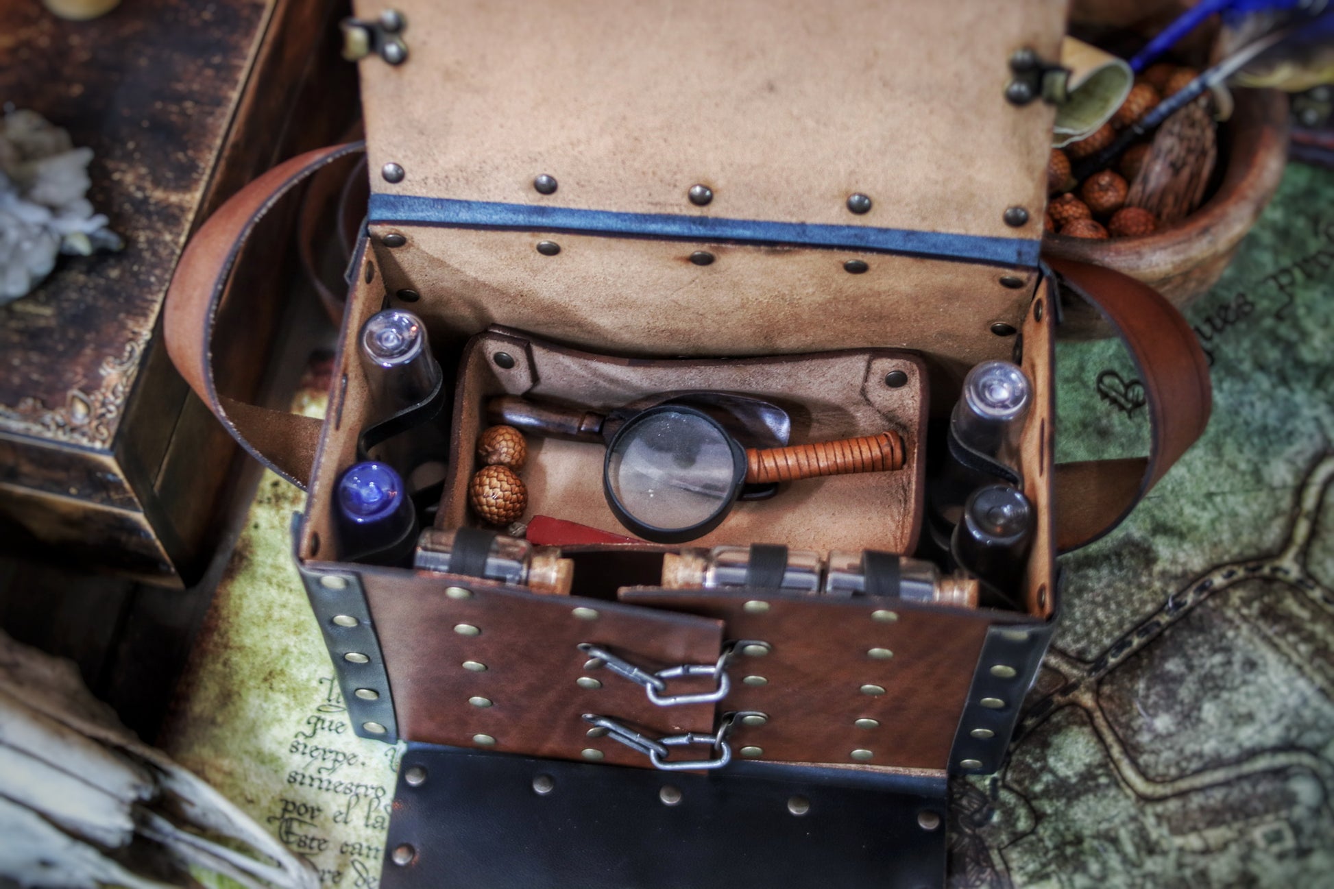 Top view of a fantasy Alchemist Leather Bag showing interior compartments with a magnifying glass, utensils, and secured potion vials. Made from natural vegetable-tanned leather, ideal for LARP, medieval cosplay, or steampunk alchemists. Practical design with a removable leather tray for tools and quick access sections for fast retrieval during roleplay adventures, battles, or magic rituals.