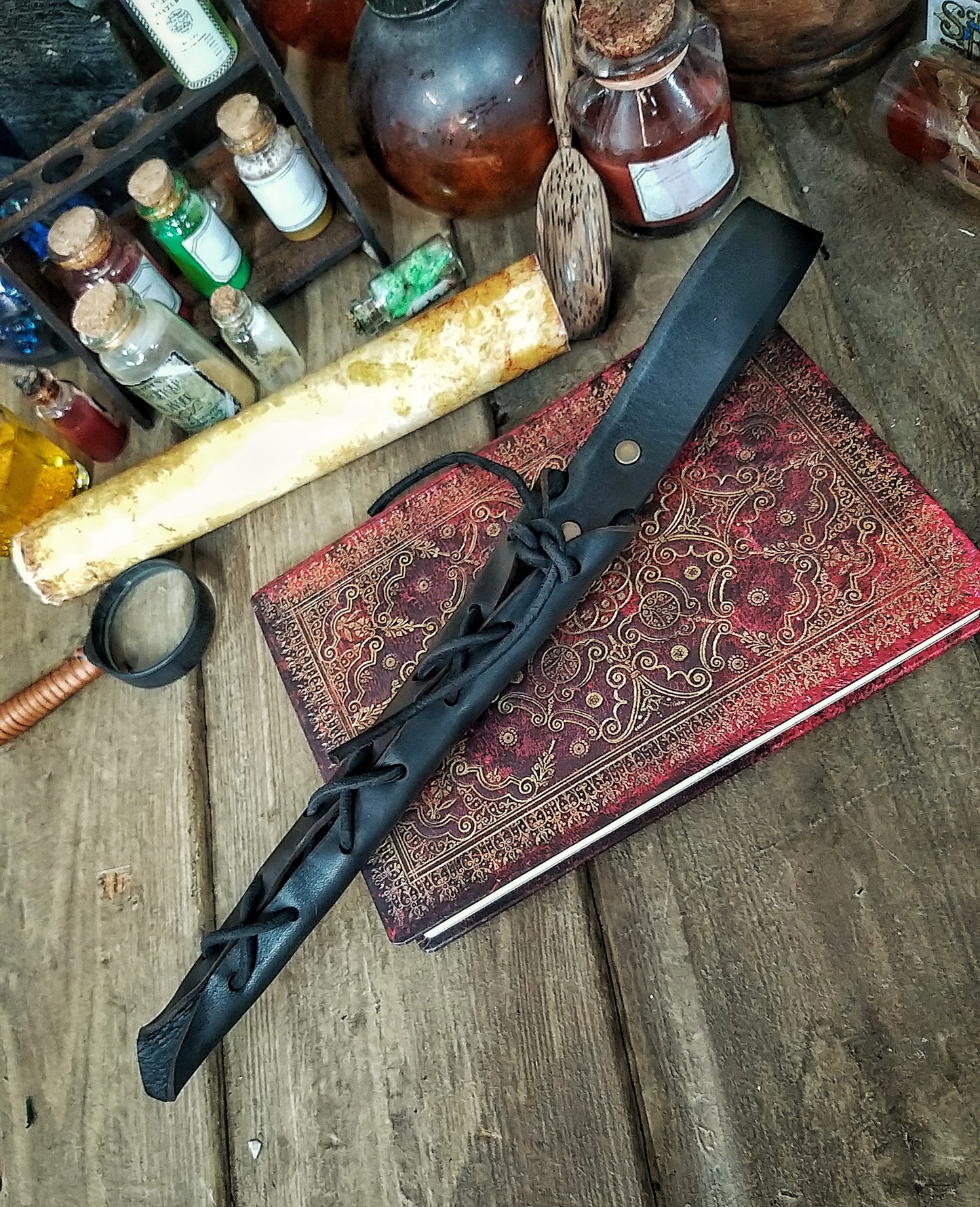 A close-up image of a brown wand holster with a leather strap and lace detail, displayed on an open book with a decorative background. Magic Wand Leather Holster Laced & Aged, perfect sheath for wizzards to hang from your belt, witch wand belt seath cosplay LARP