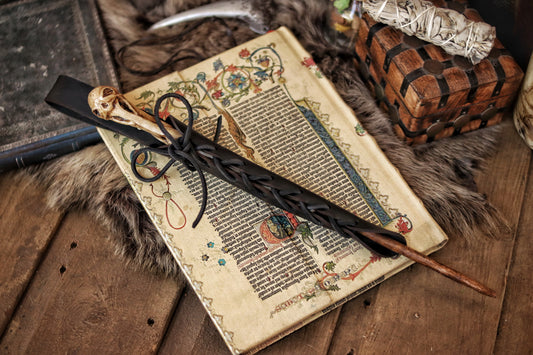 A close-up image of a brown wand holster with a leather strap and lace detail, displayed on an open book with a decorative background. Magic Wand Leather Holster Laced & Aged, perfect sheath for wizzards to hang from your belt, witch wand belt seath cosplay LARP