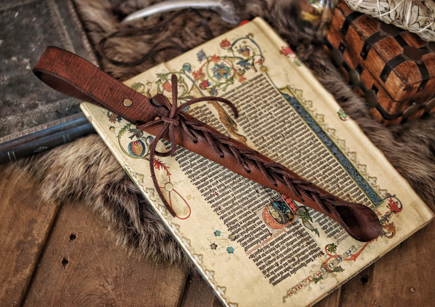 A close-up image of a brown wand holster with a leather strap and lace detail, displayed on an open book with a decorative background. Magic Wand Leather Holster Laced & Aged, perfect sheath for wizzards to hang from your belt, witch wand belt seath cosplay LARP