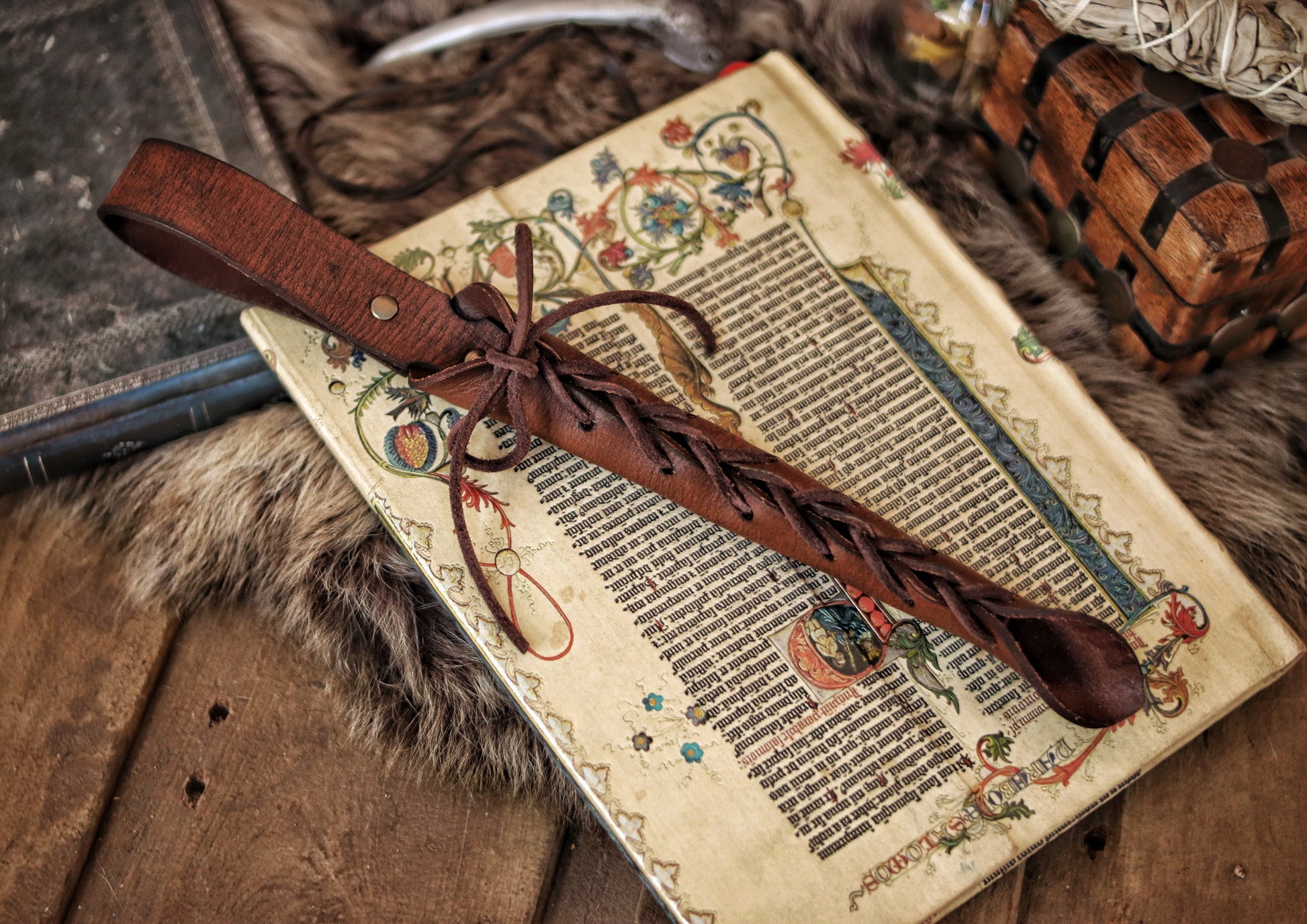 A close-up image of a brown wand holster with a leather strap and lace detail, displayed on an open book with a decorative background. Magic Wand Leather Holster Laced & Aged, perfect sheath for wizzards to hang from your belt, witch wand belt seath cosplay LARP